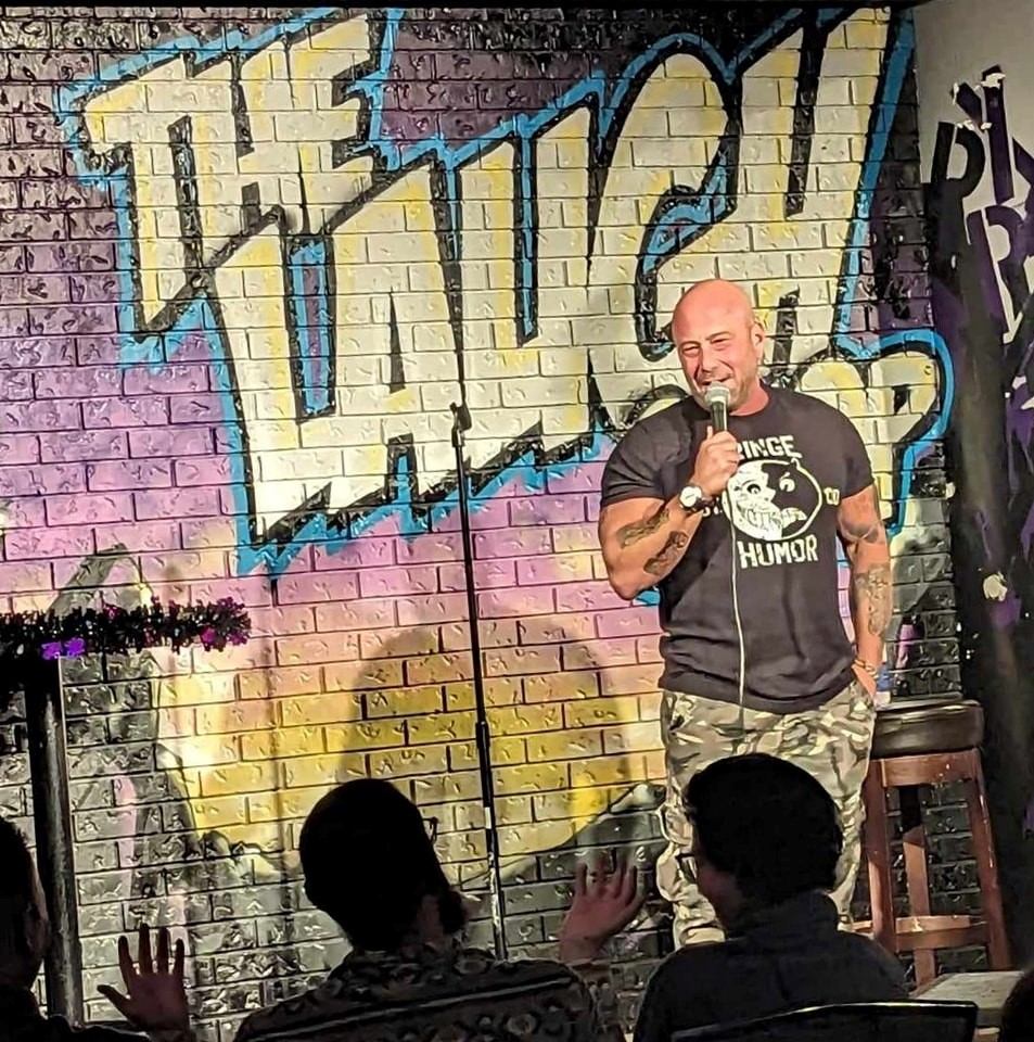 Comedian on stage at The Laugh Shop with graffiti brick wall.
