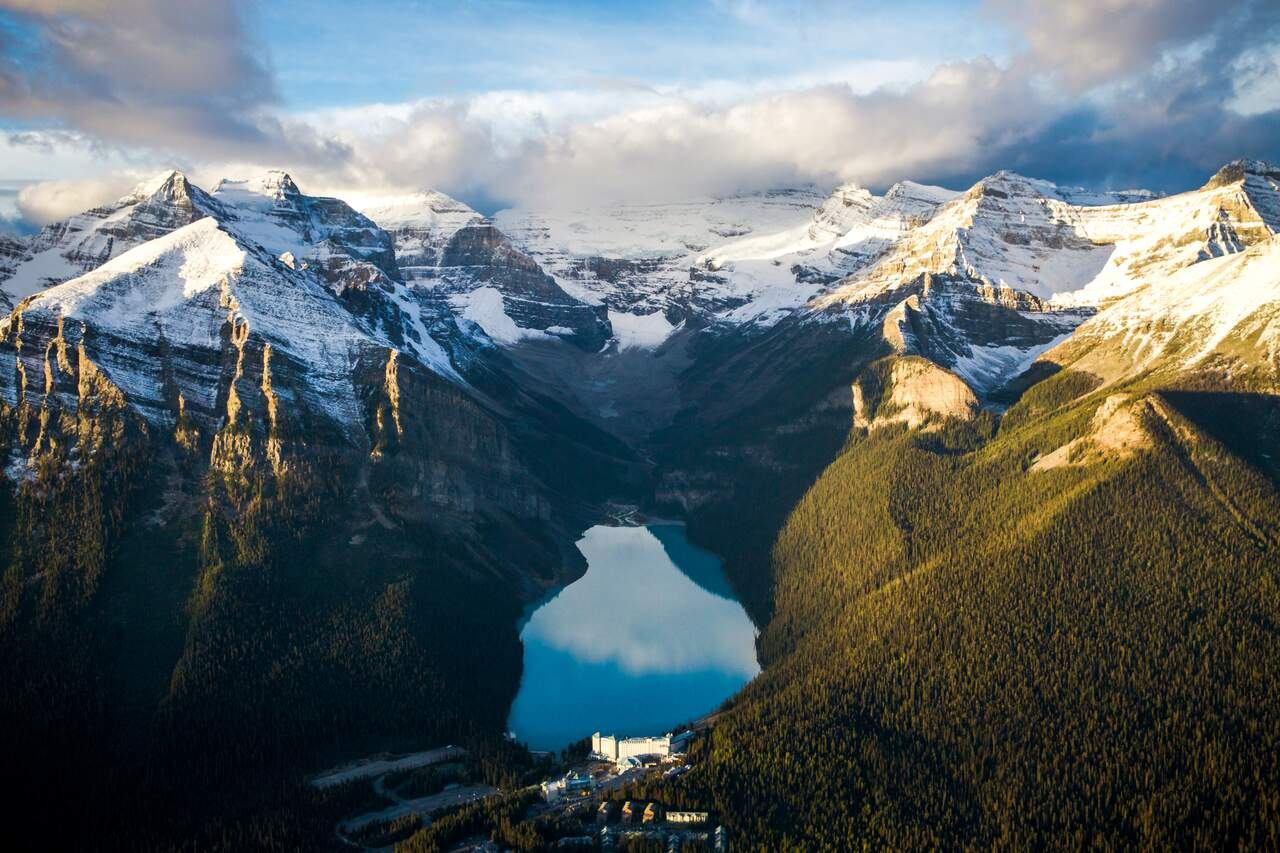 Aerial sunset view of Lake Louise surrounded by snow-capped peaks and dense evergreen forests.