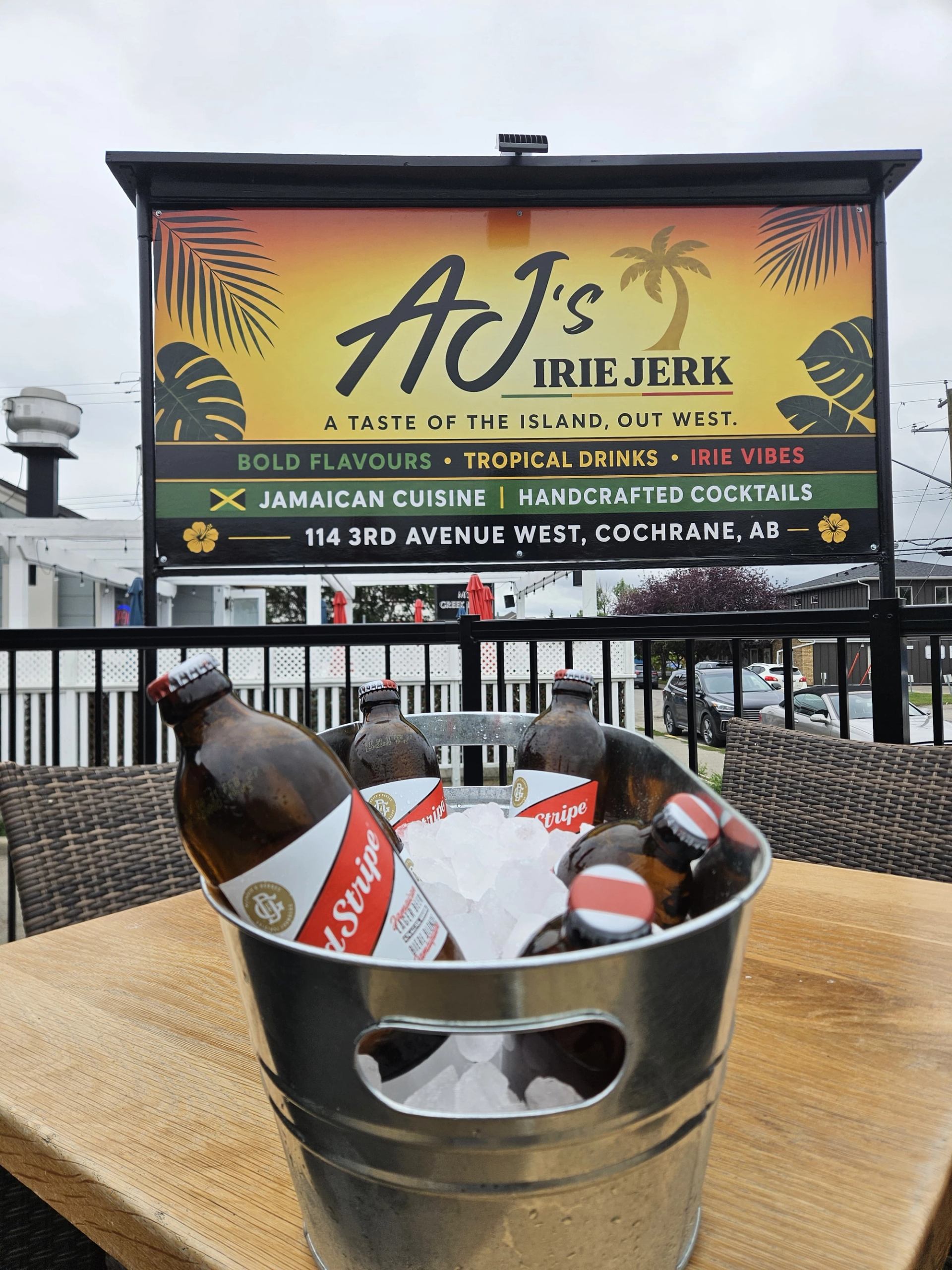 Bucket of Red Stripe bottles on ice beneath AJ's Irie Jerk patio sign.
