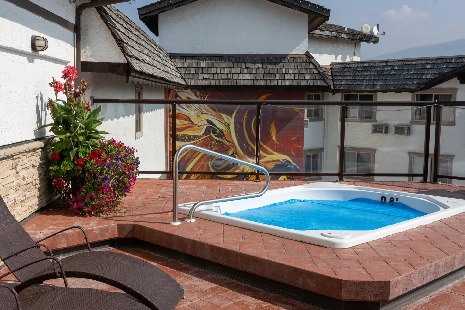 Rooftop terrace with hot tub, lounge chairs, mural, and potted flowers.