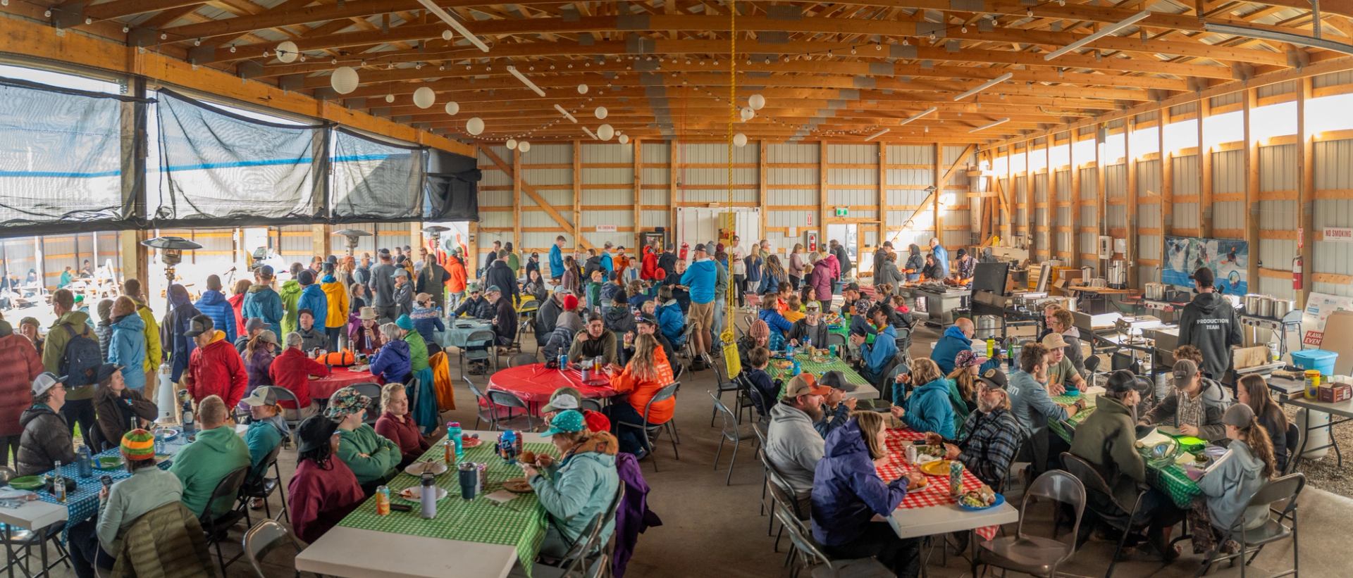 Large indoor gathering with people seated at tables for a community meal.