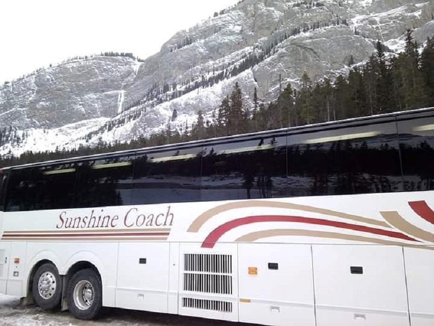Sunshine Coach bus with red and gold design in front of snowy mountains and forest.