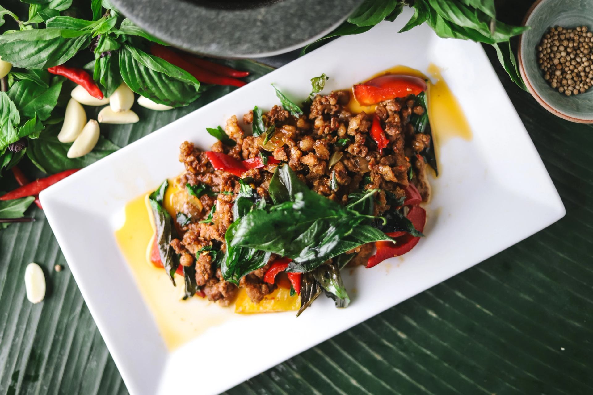 Stir-fried minced meat with basil and red peppers on white plate, herbs beside.