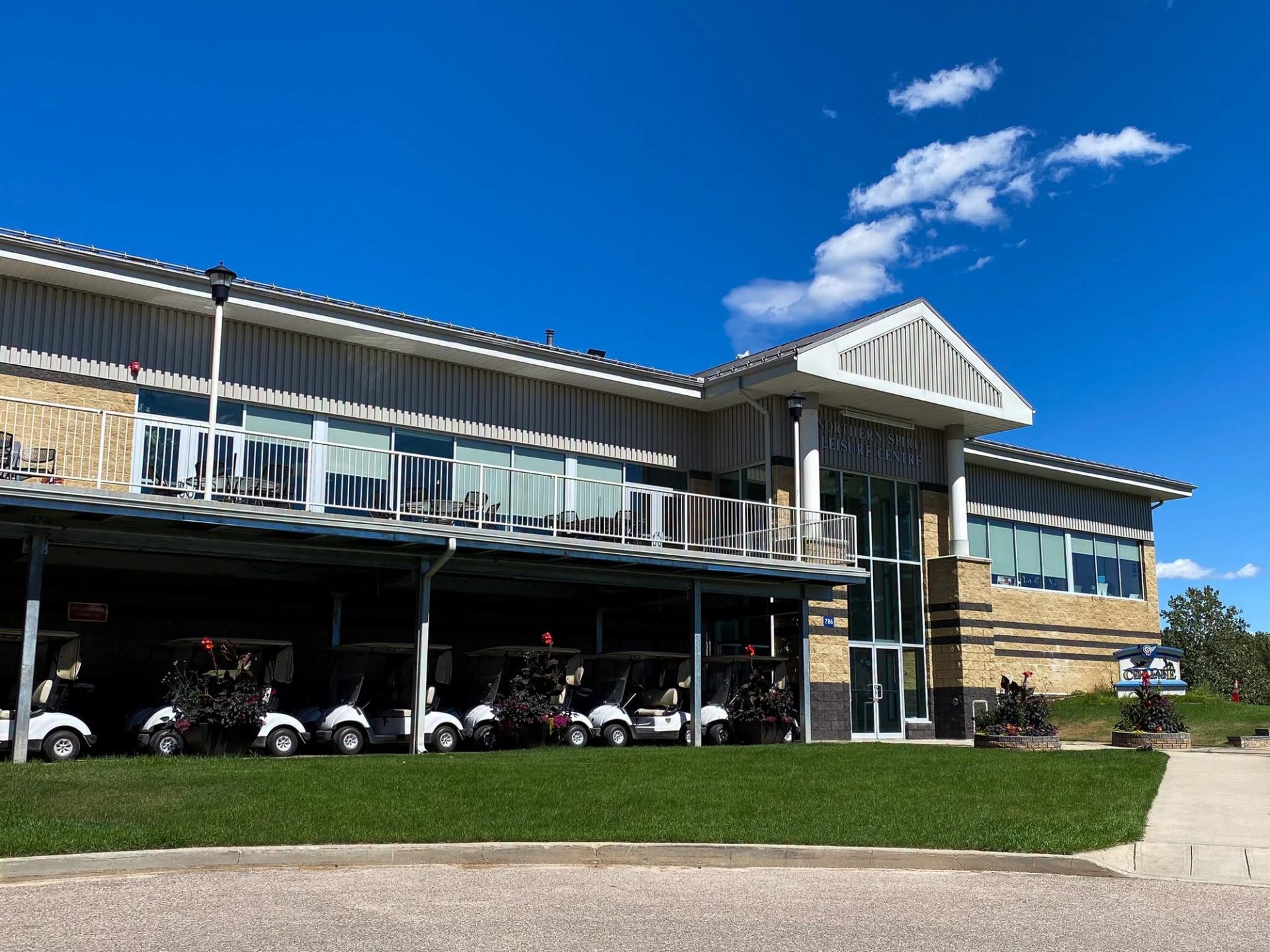 Golf clubhouse with upper patio, parked golf carts below, under clear blue sky.