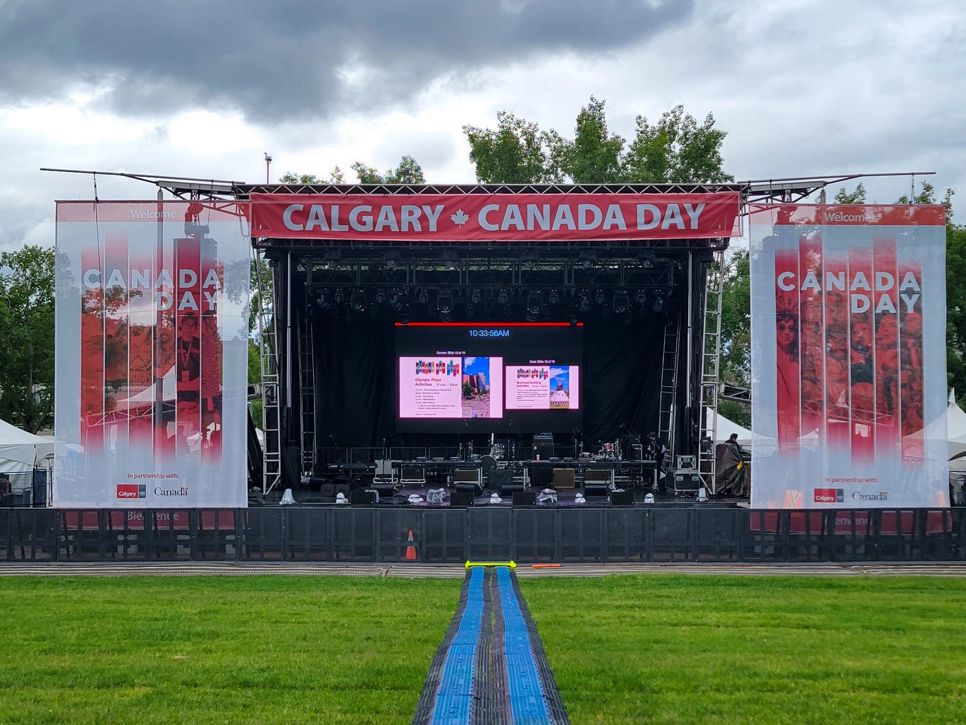 Outdoor Calgary Canada Day concert stage with large banners and empty grassy audience area.