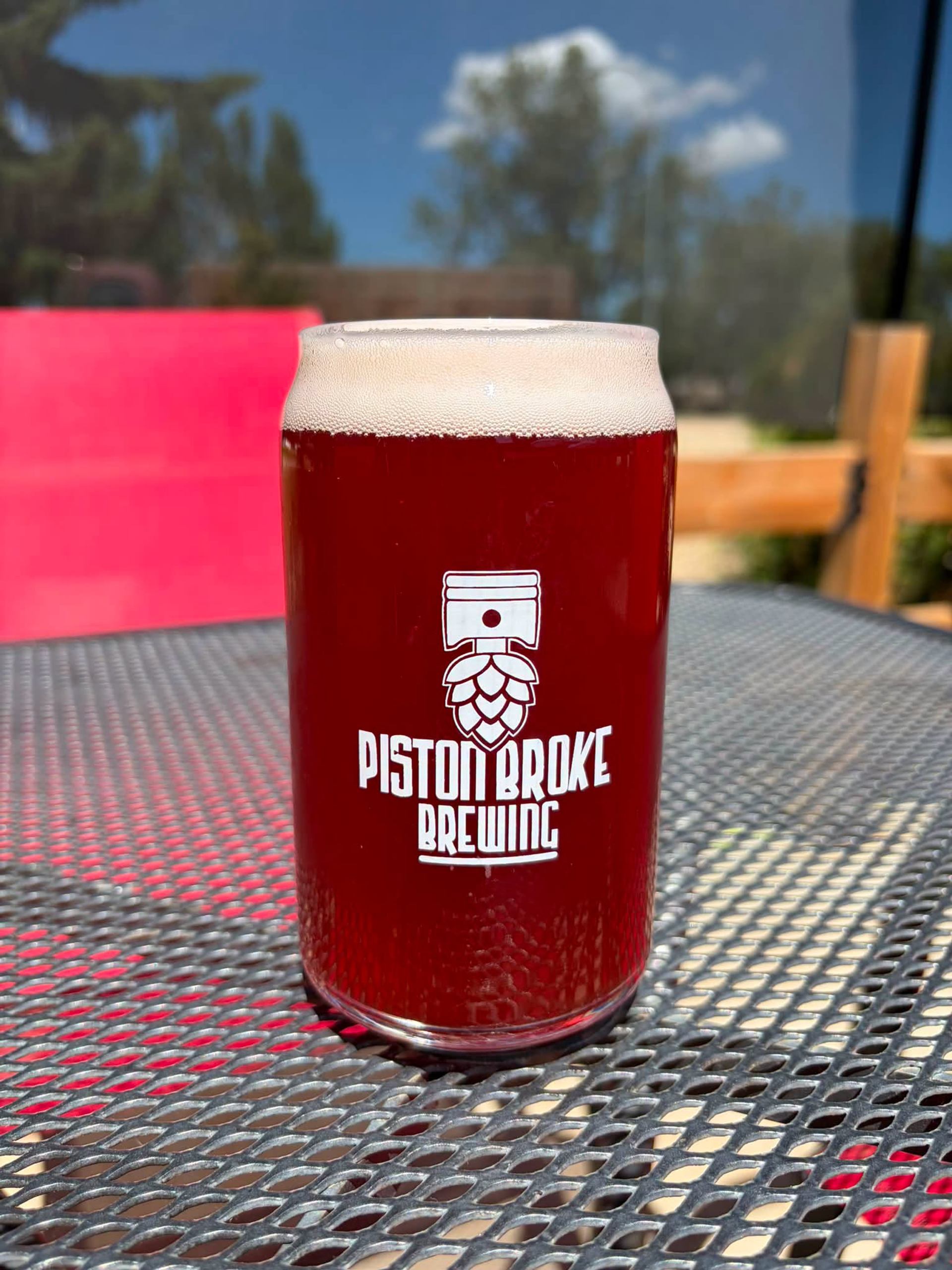 Piston Broke Brewing serves a vibrant red beer in a branded glass on the outdoor patio.