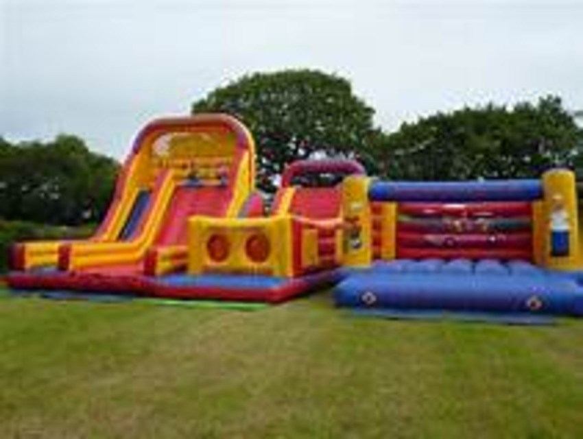 Colorful inflatable obstacle course and slides set up on grass for a community event.