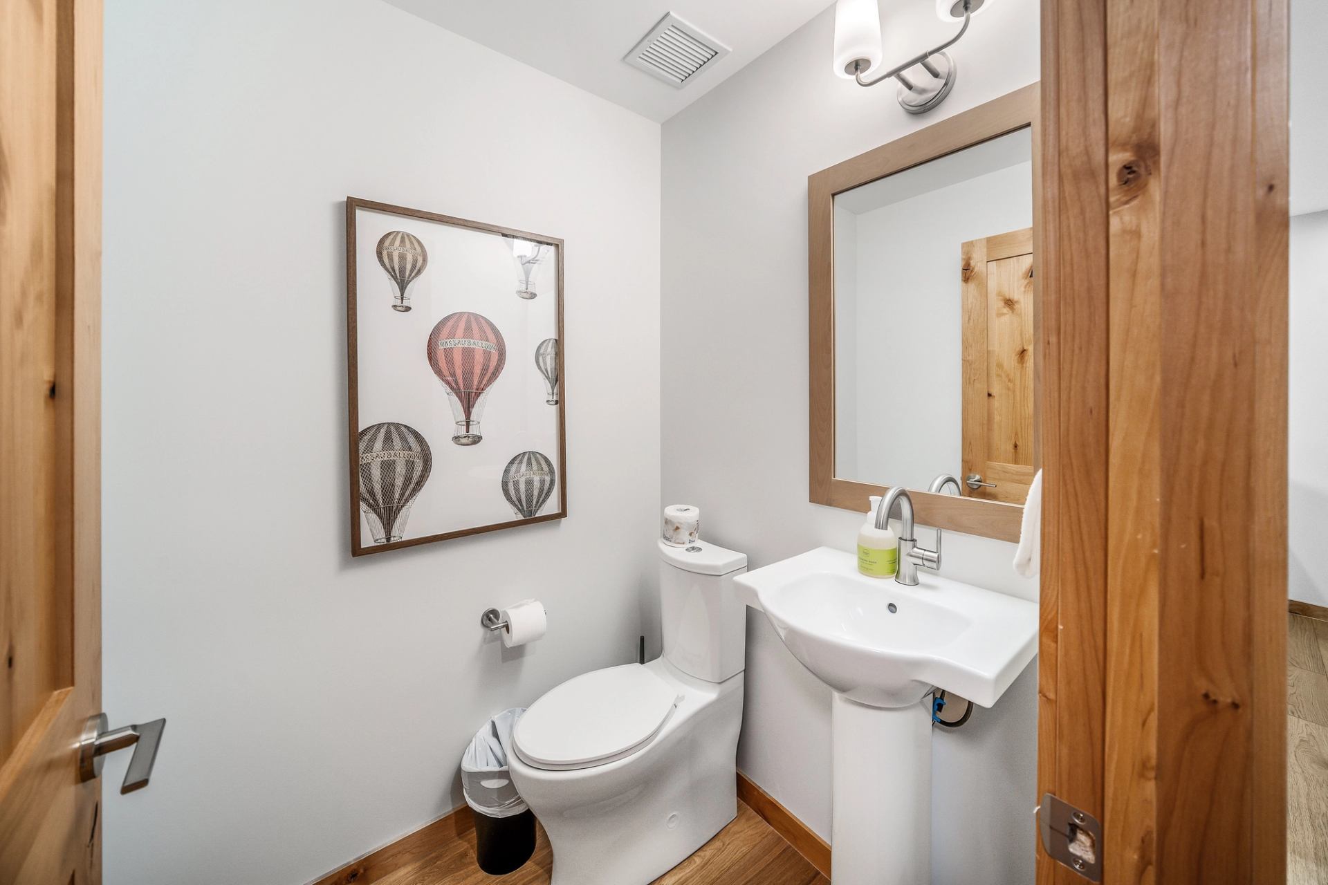 Small bathroom with pedestal sink, toilet, hot air balloon artwork and wood accents.
