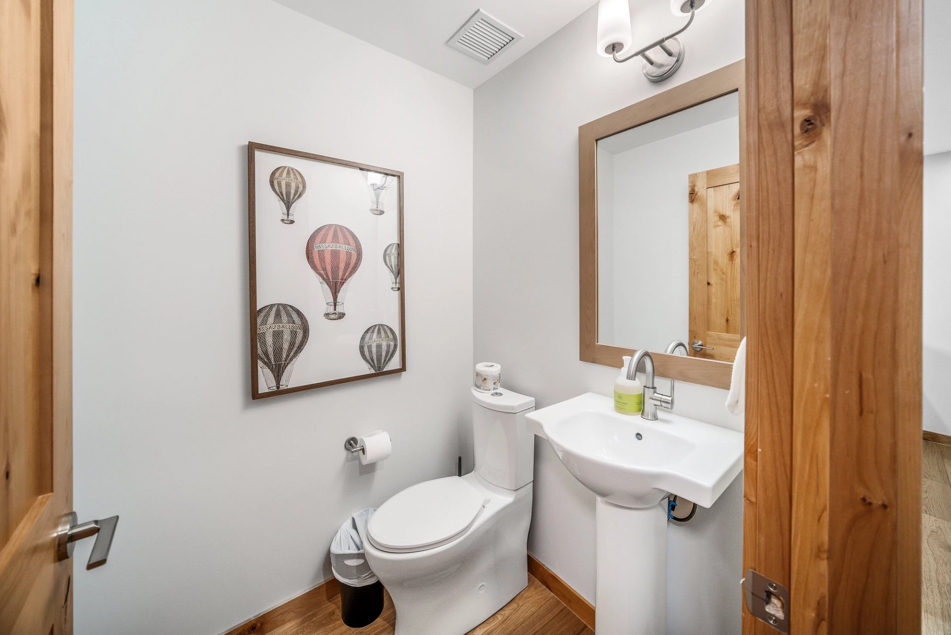 Small bathroom with pedestal sink, toilet, hot air balloon artwork and wood accents.