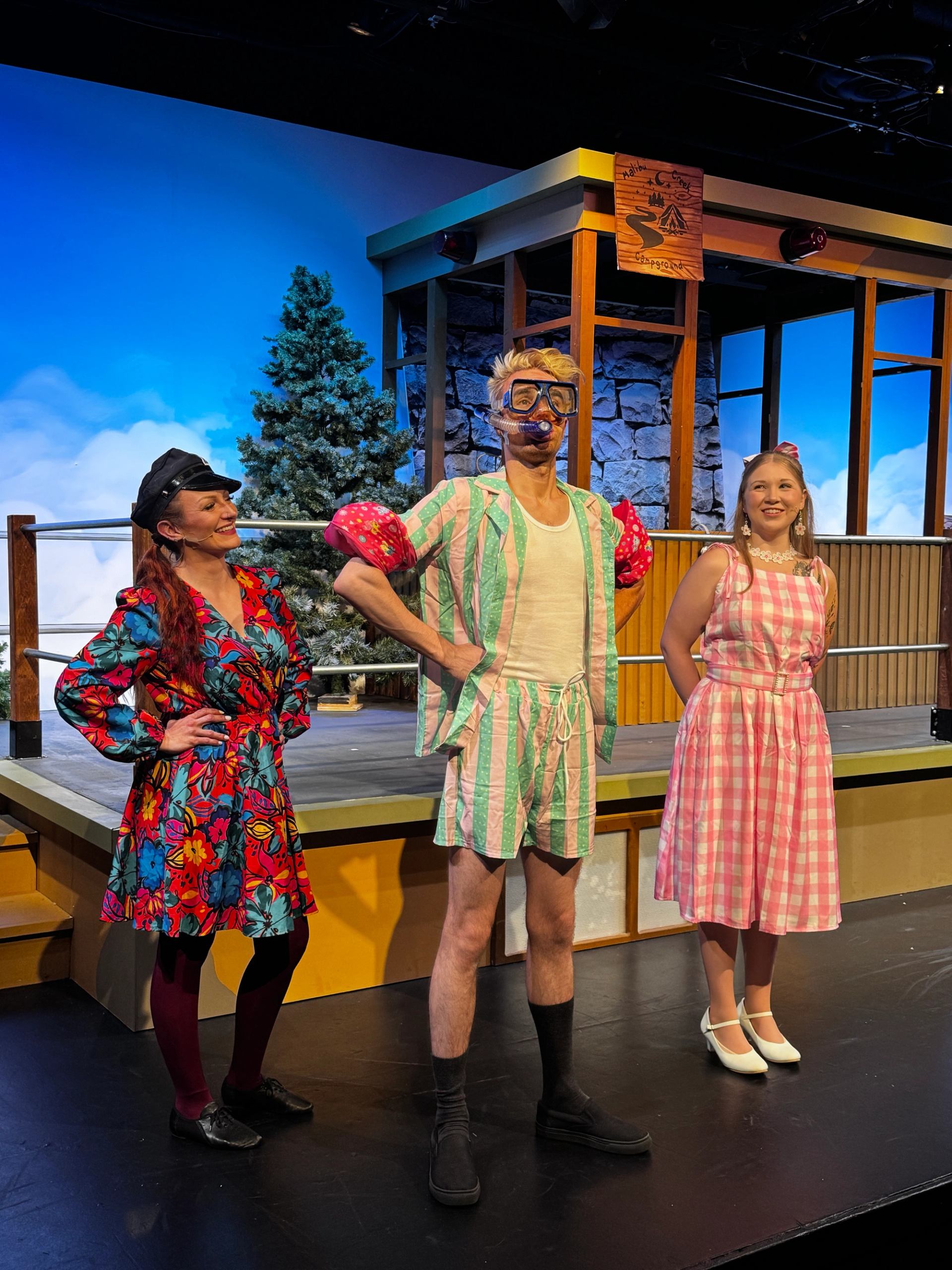 Three performers in bright costumes standing on a stage with a winter backdrop.