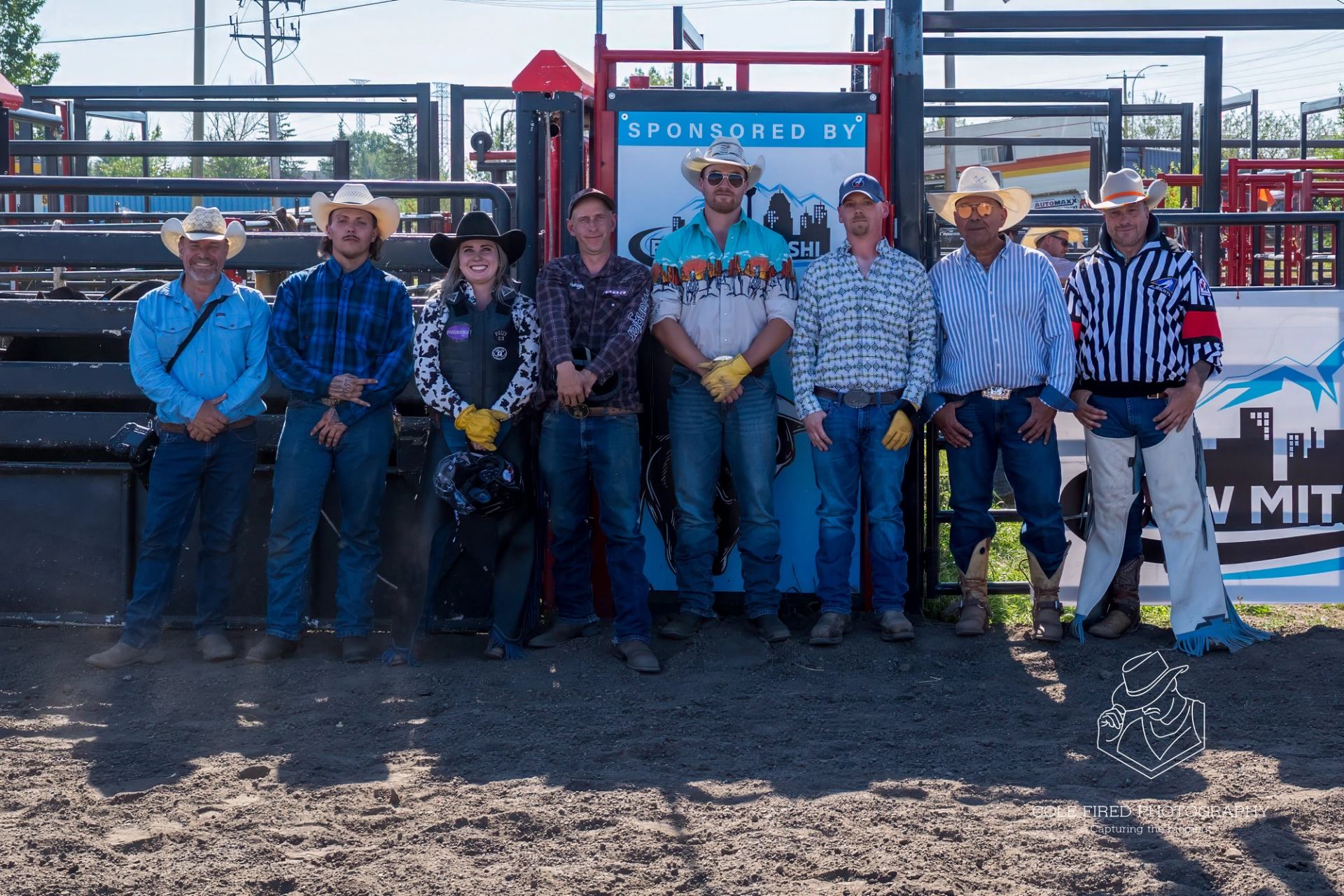 Rodeo lineup posing beside sponsored bull riding arena gate and backdrop, Calgary, Alberta.