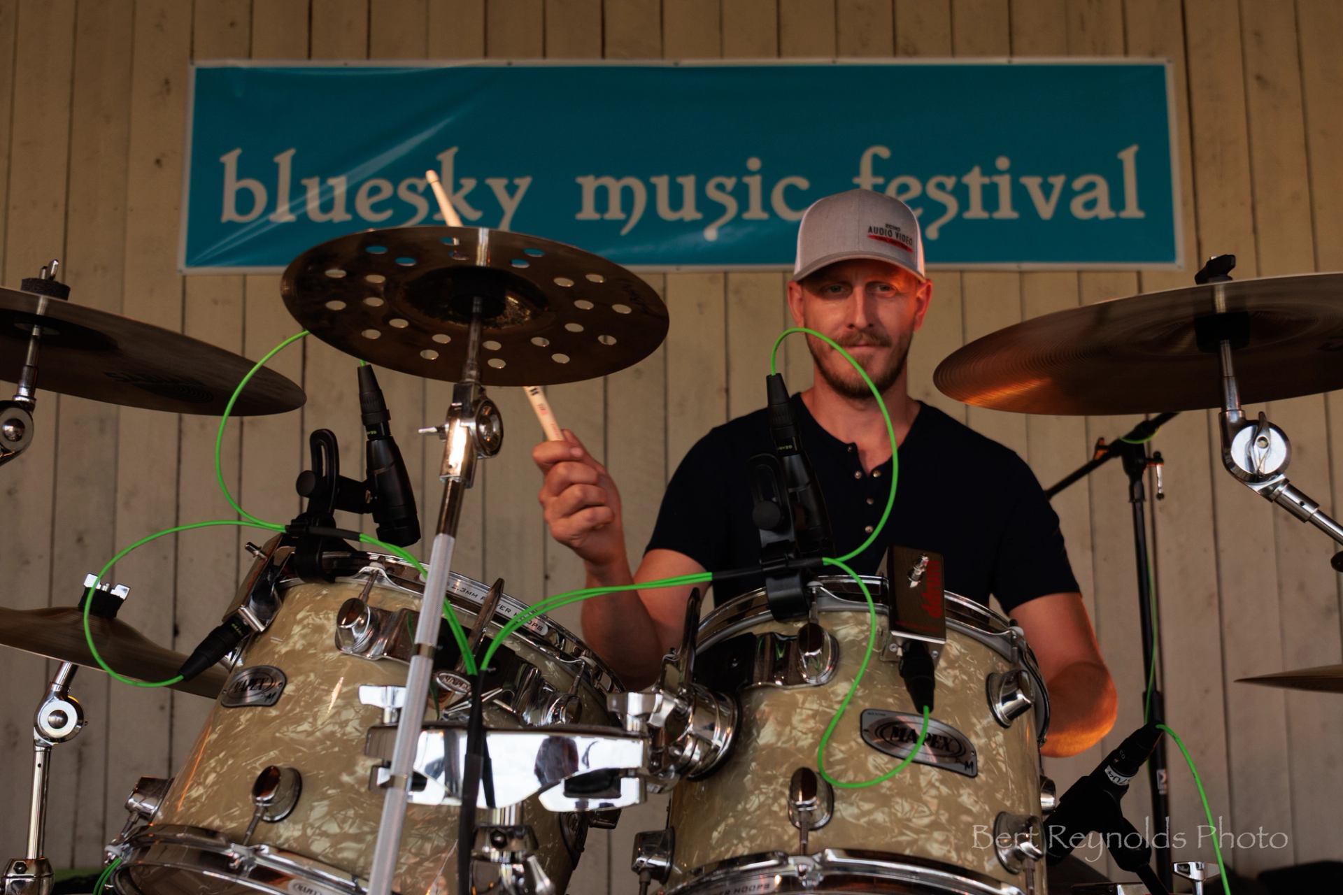 Drummer playing a drum kit onstage under a Bluesky Music Festival banner.