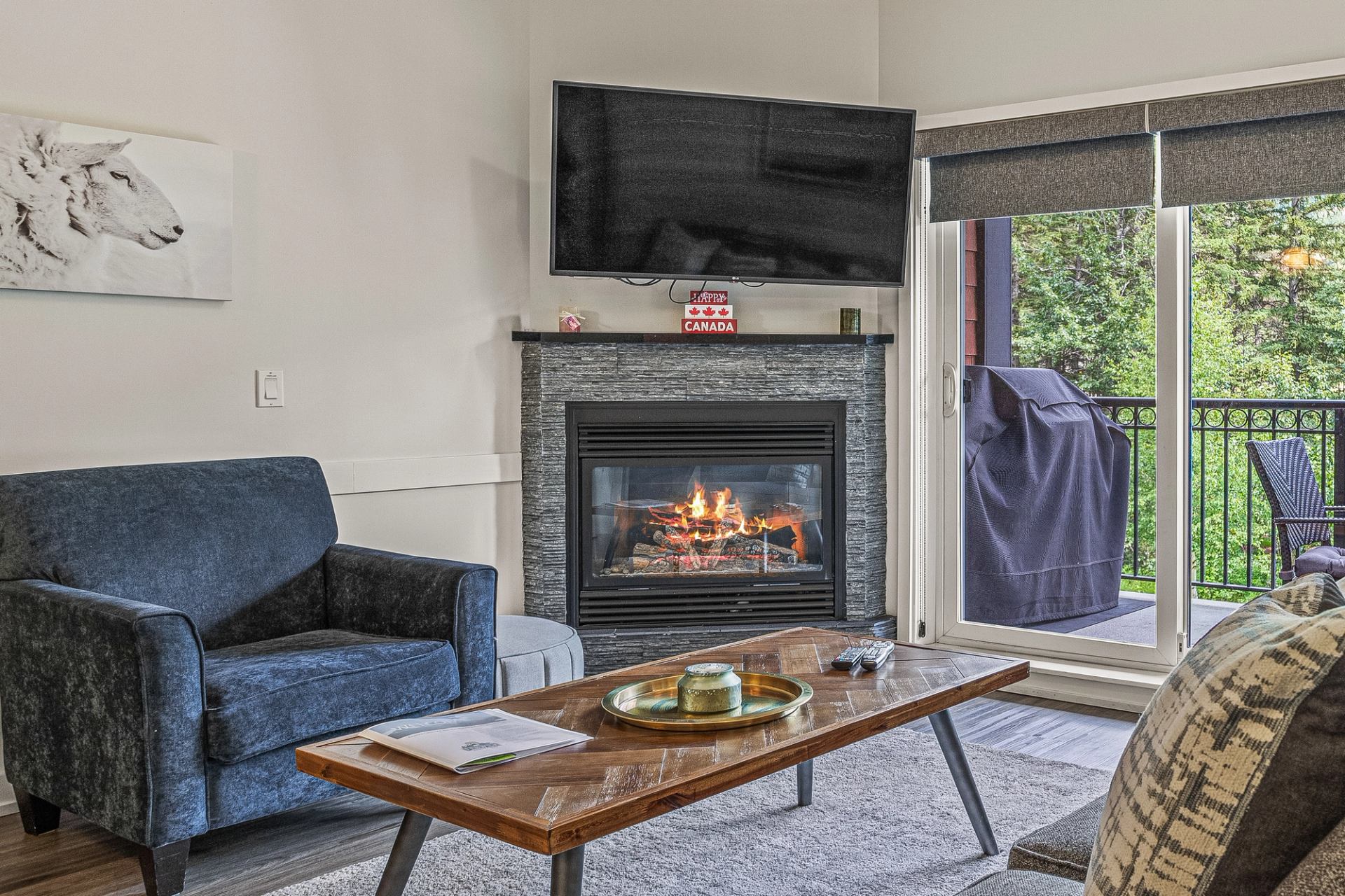 Living room with blue armchair, lit fireplace, wall-mounted TV and balcony doors.