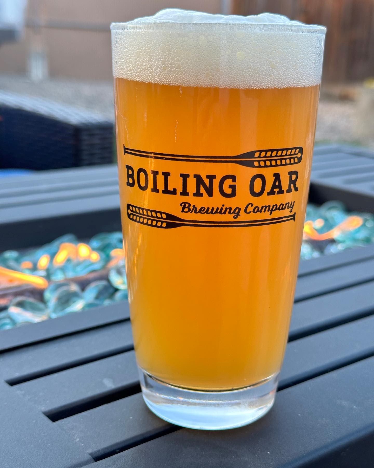 Beer glass with “Boiling Oar Brewing Company” logo and foamy head on a table.