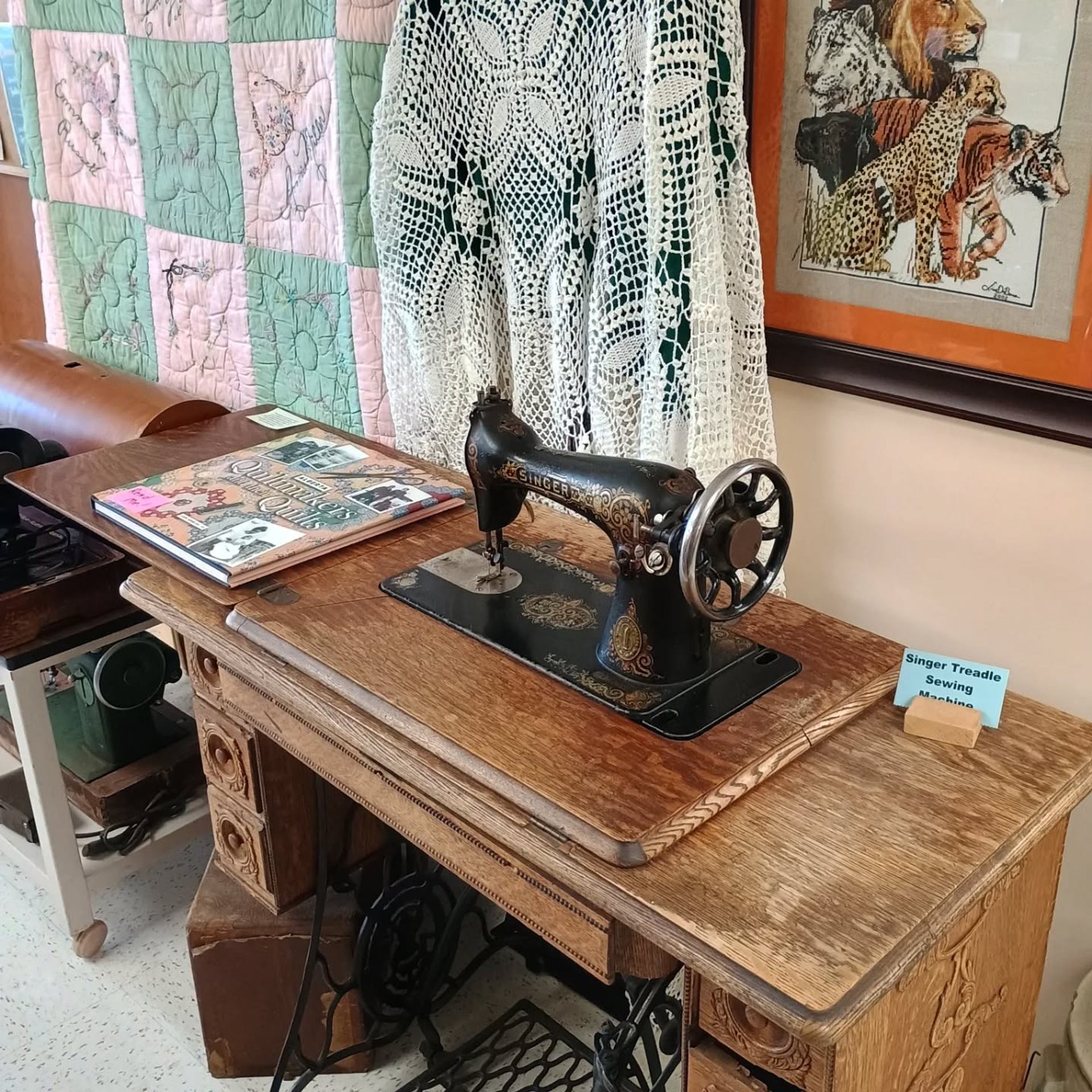 Antique Singer sewing machine on ornate wooden table with quilts behind