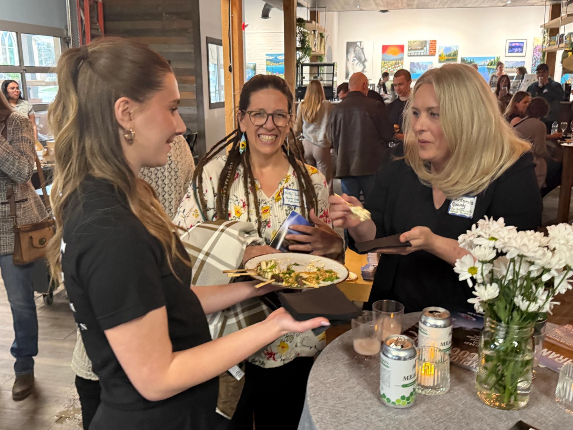 People stand around a small table, eating appetizers and talking at an indoor event.