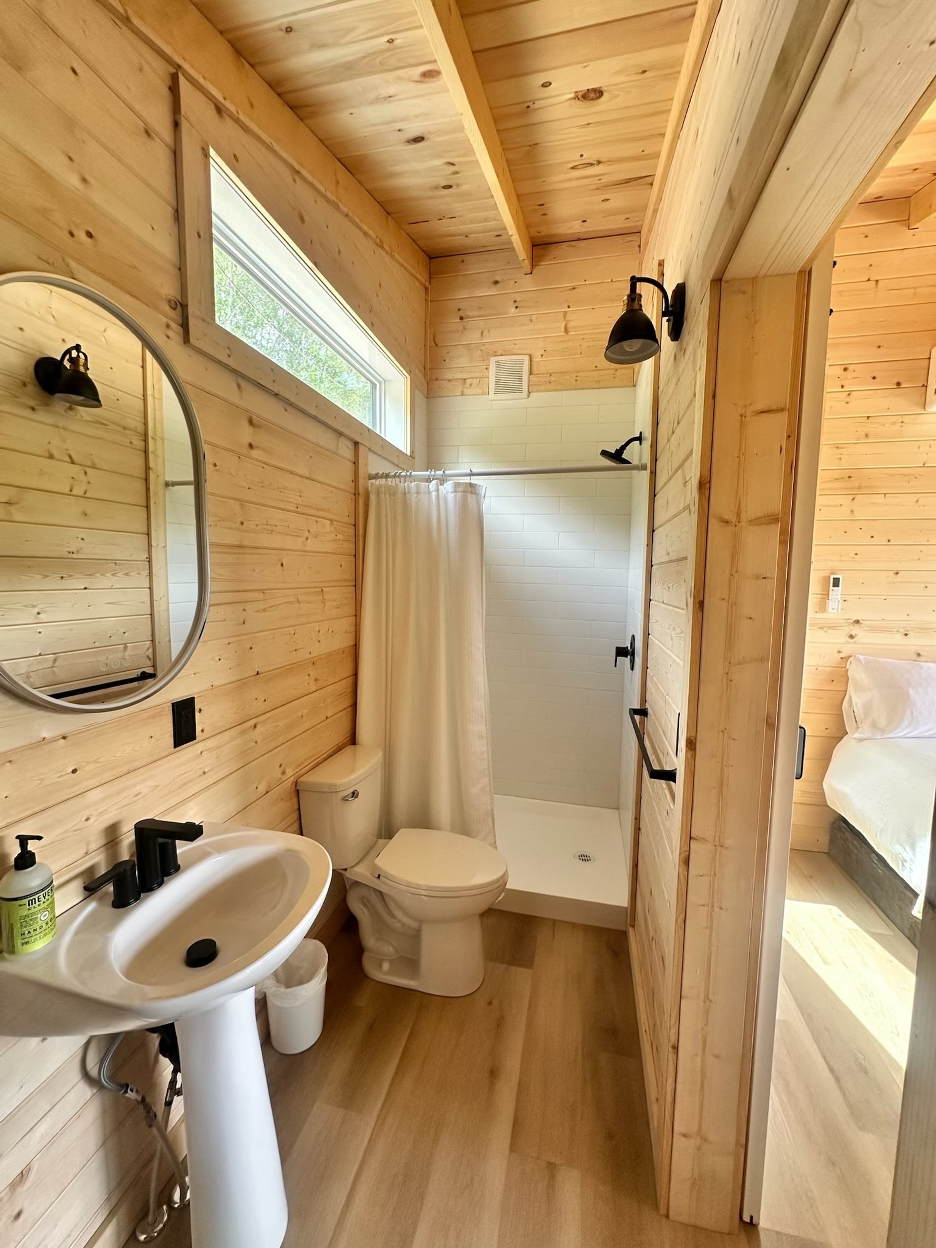 Small cabin bathroom with wood walls, a pedestal sink, toilet, and shower with a white curtain.
