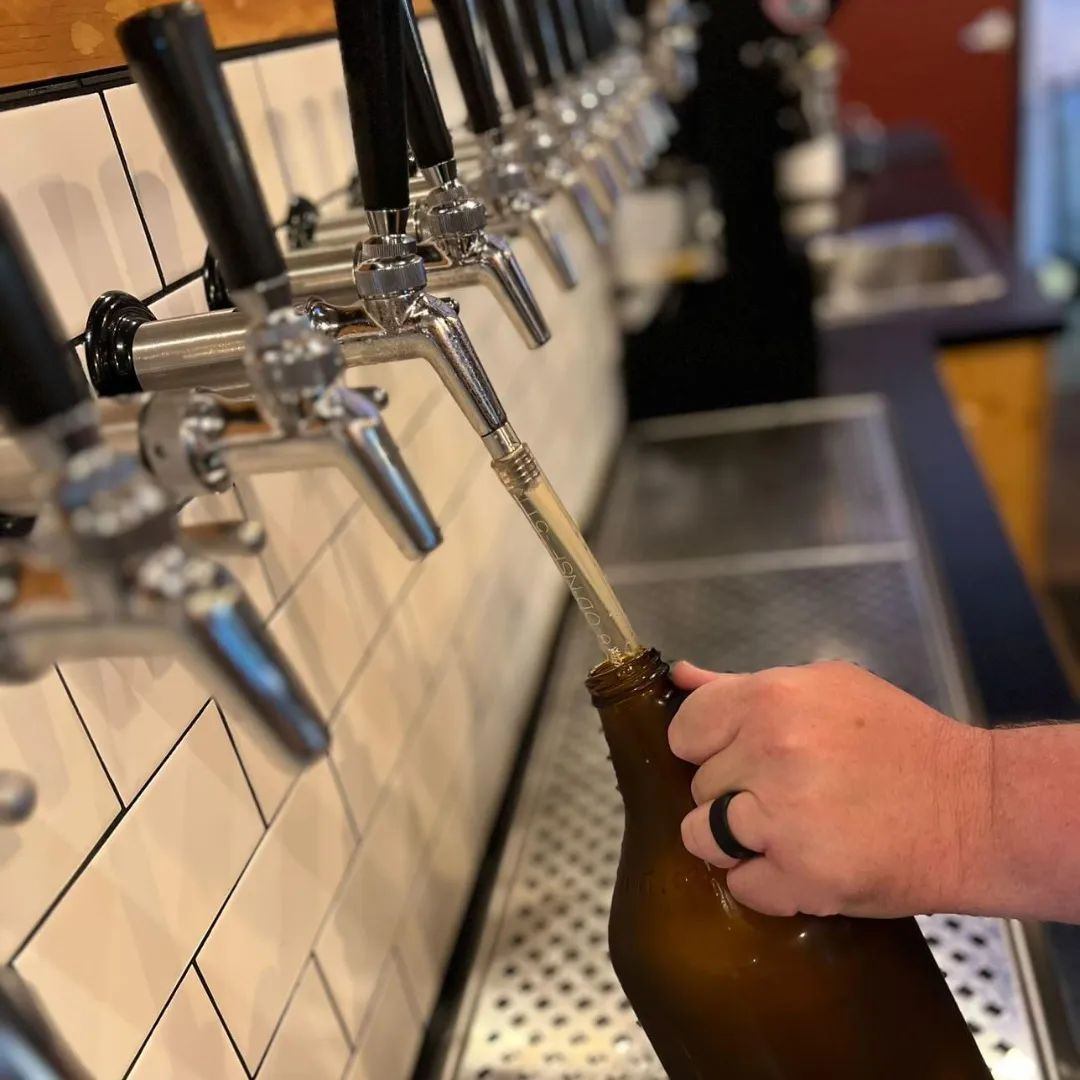 Hand filling a brown growler directly from a stainless steel beer tap