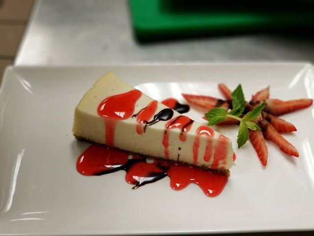 Cheesecake slice with strawberry sauce, chocolate drizzle, sliced strawberries and mint.