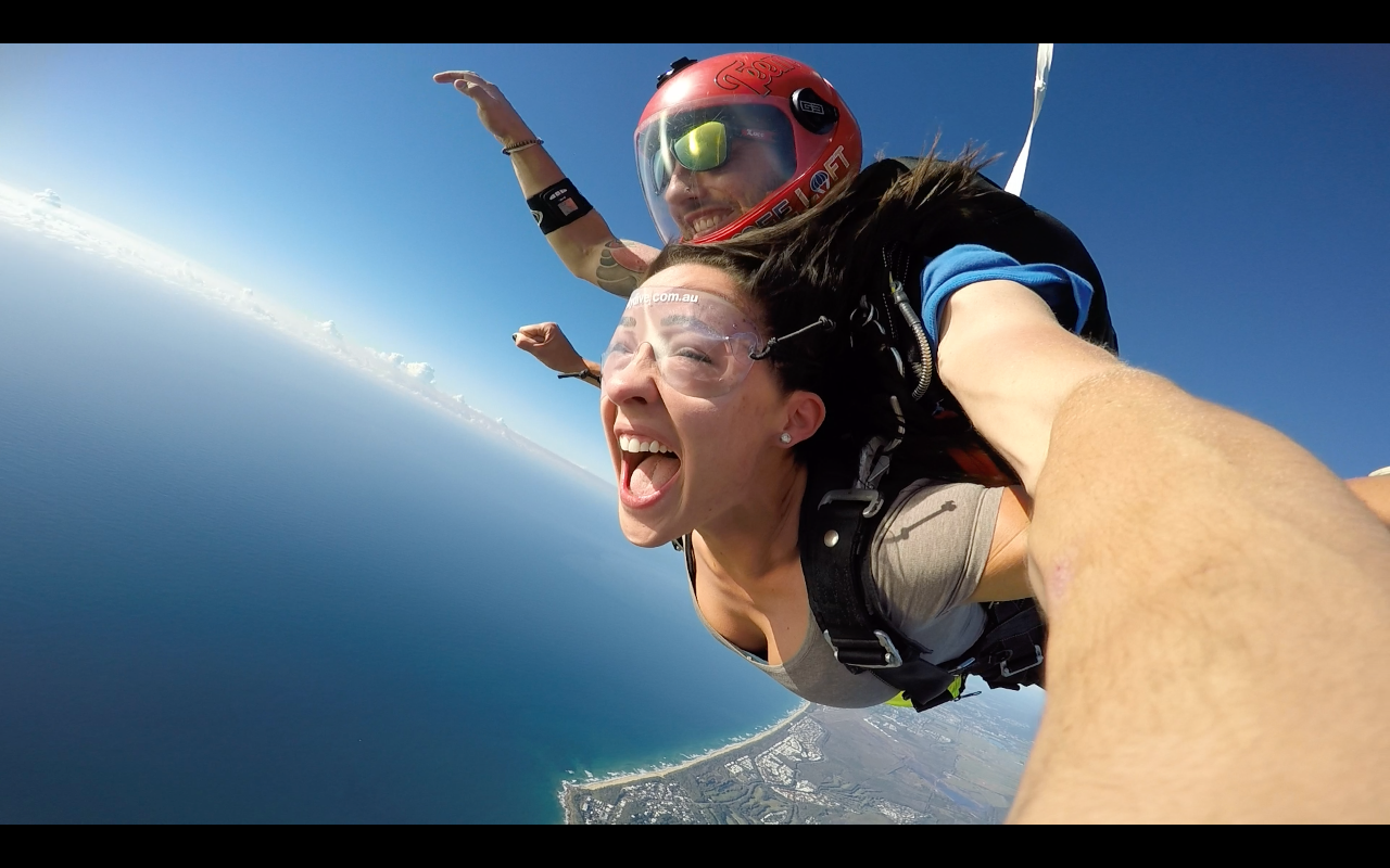 Two people tandem skydiving over the coastline with wide open sky.