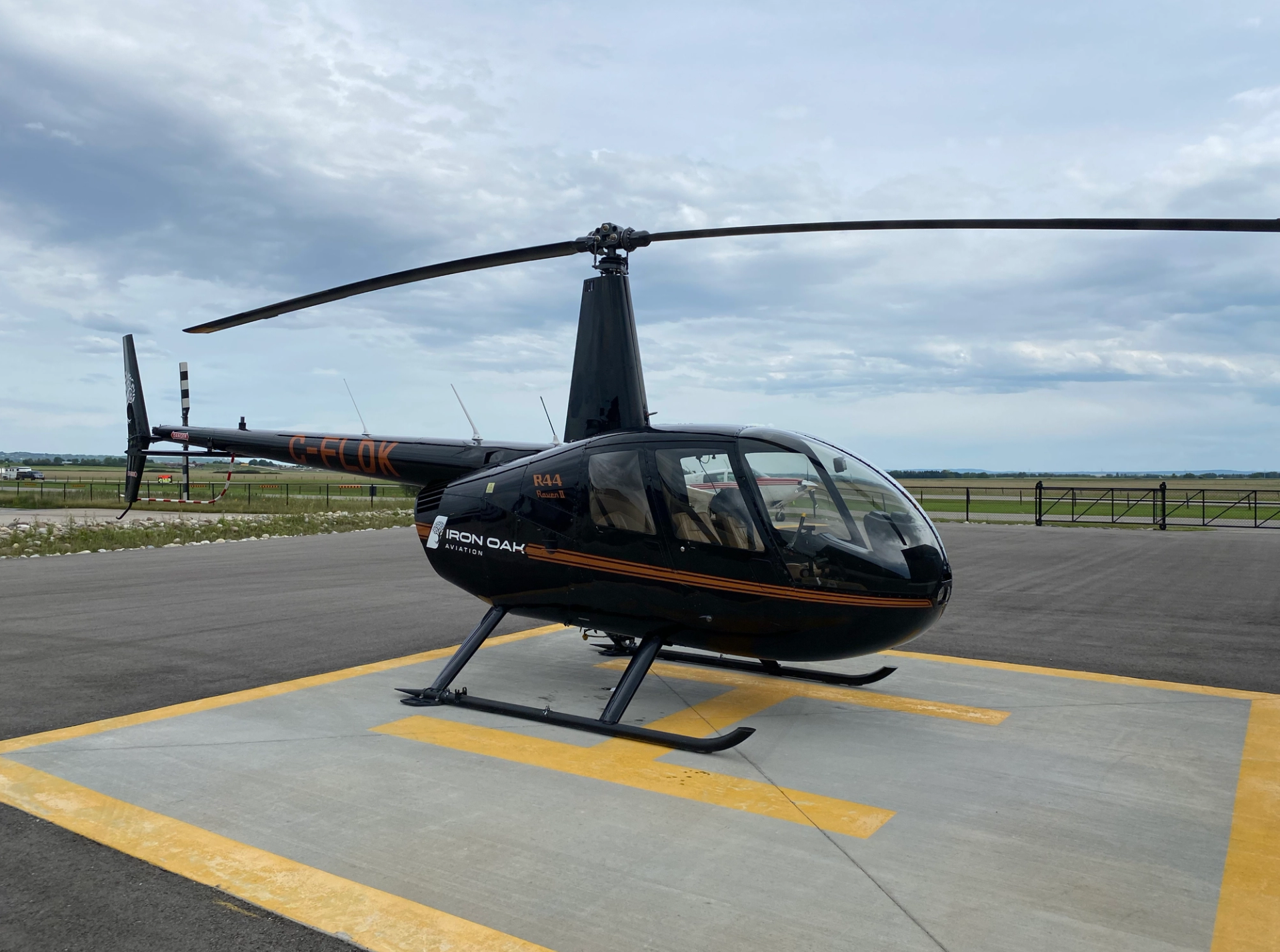 Black Iron Oak Aviation helicopter parked on helipad beside runway and grassy airfield.