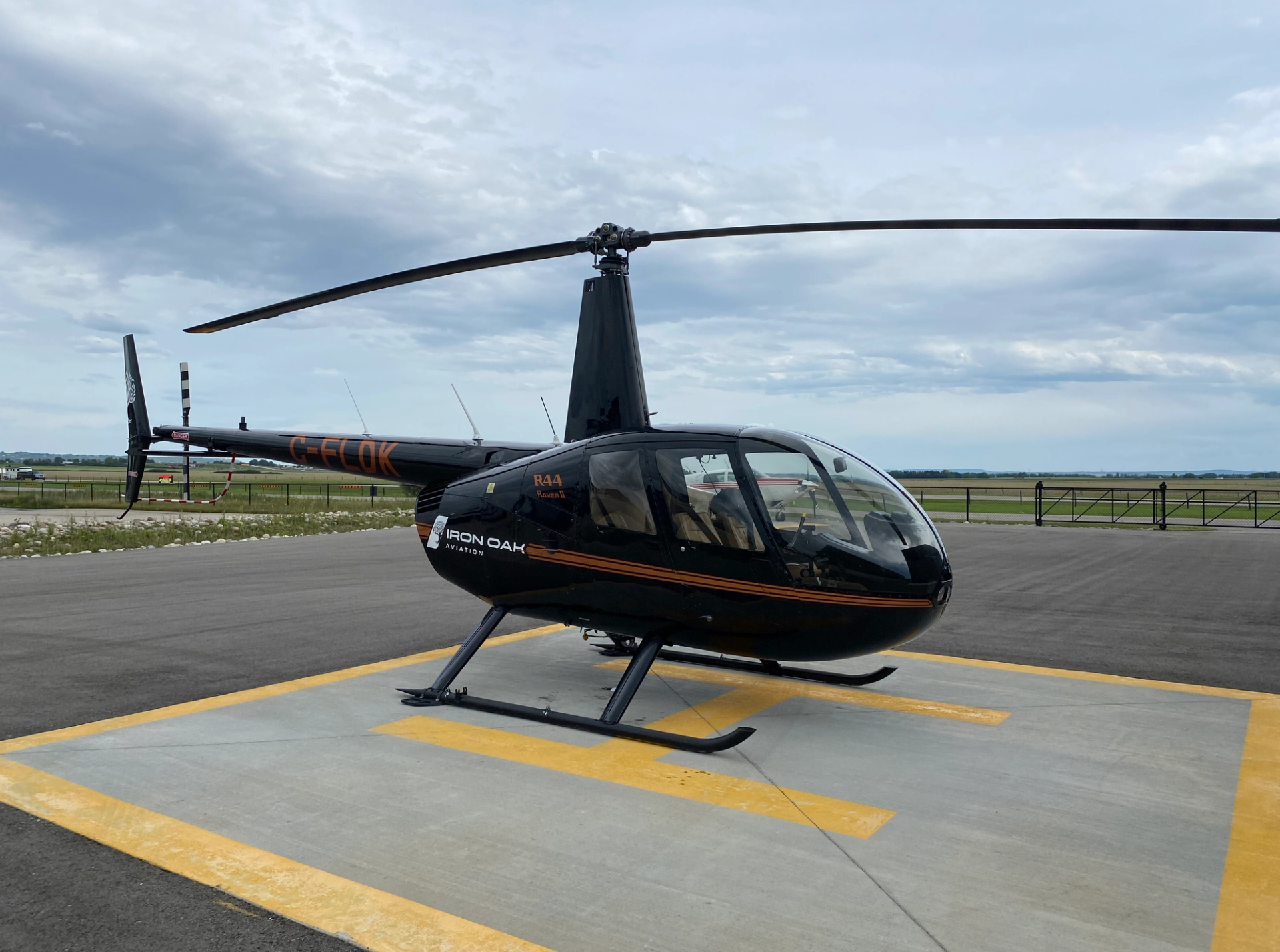 Black Iron Oak Aviation helicopter parked on helipad beside runway and grassy airfield.