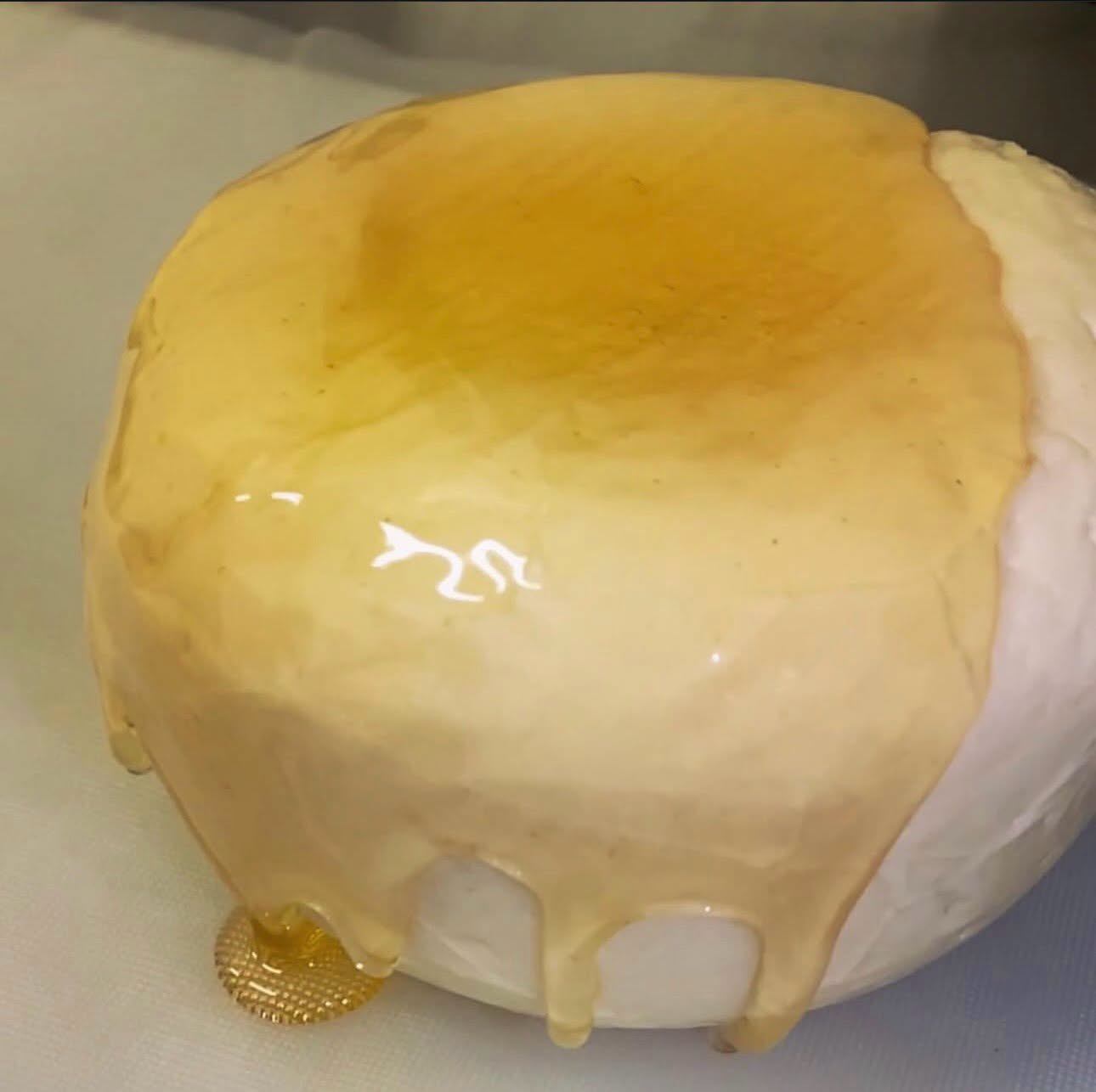 A wheel of cheese is coated with a glossy golden glaze that drips down the sides.