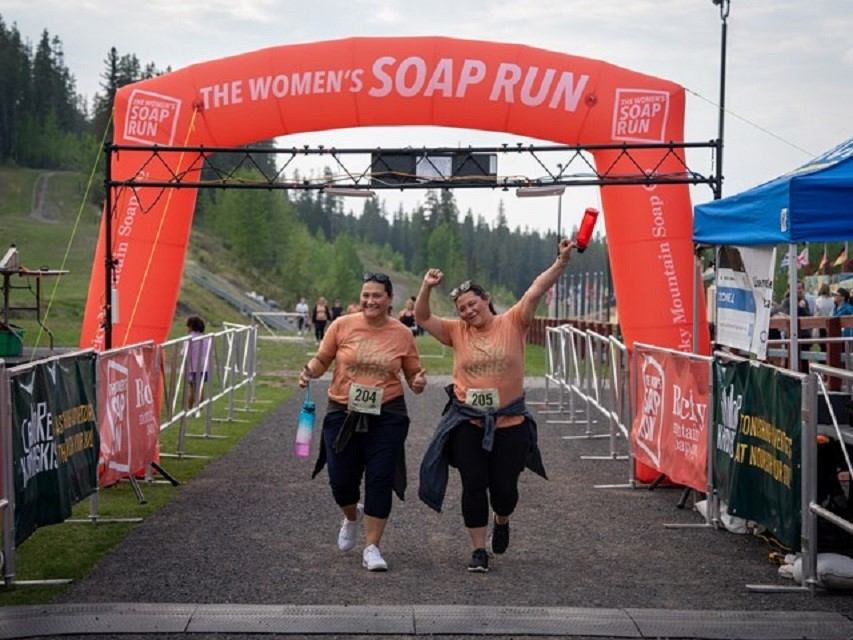 Finish line arch reading “The Women’s Soap Run” with two runners raising arms.