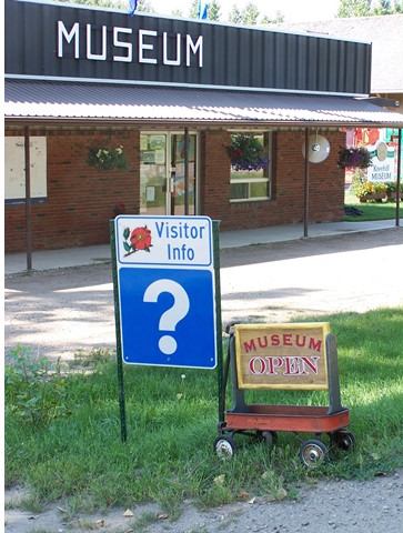 Museum building with MUSEUM sign, visitor info sign, and wagon reading MUSEUM OPEN.
