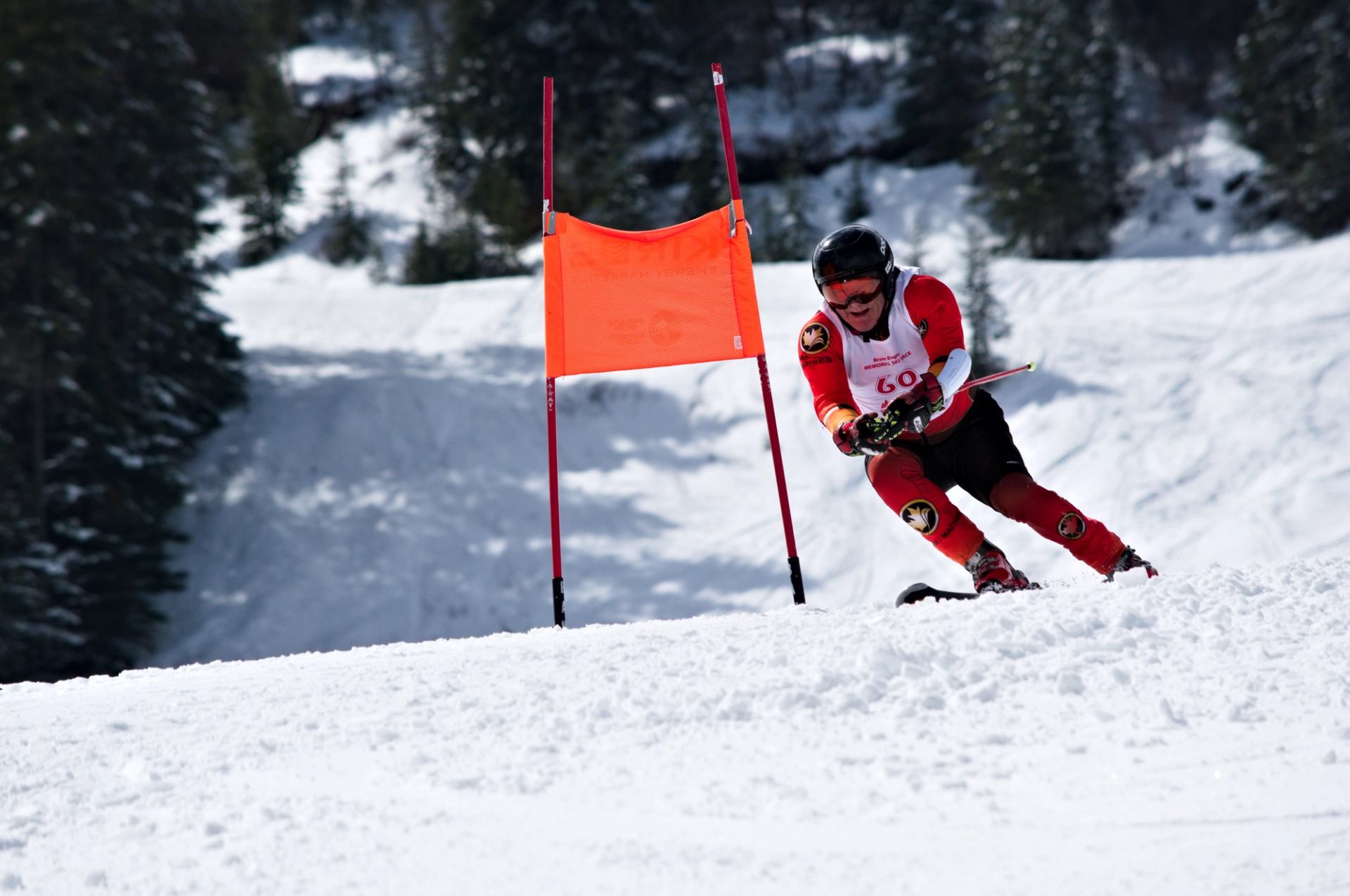 Skier in red racing suit carves through snow past an orange gate on a mountain course.