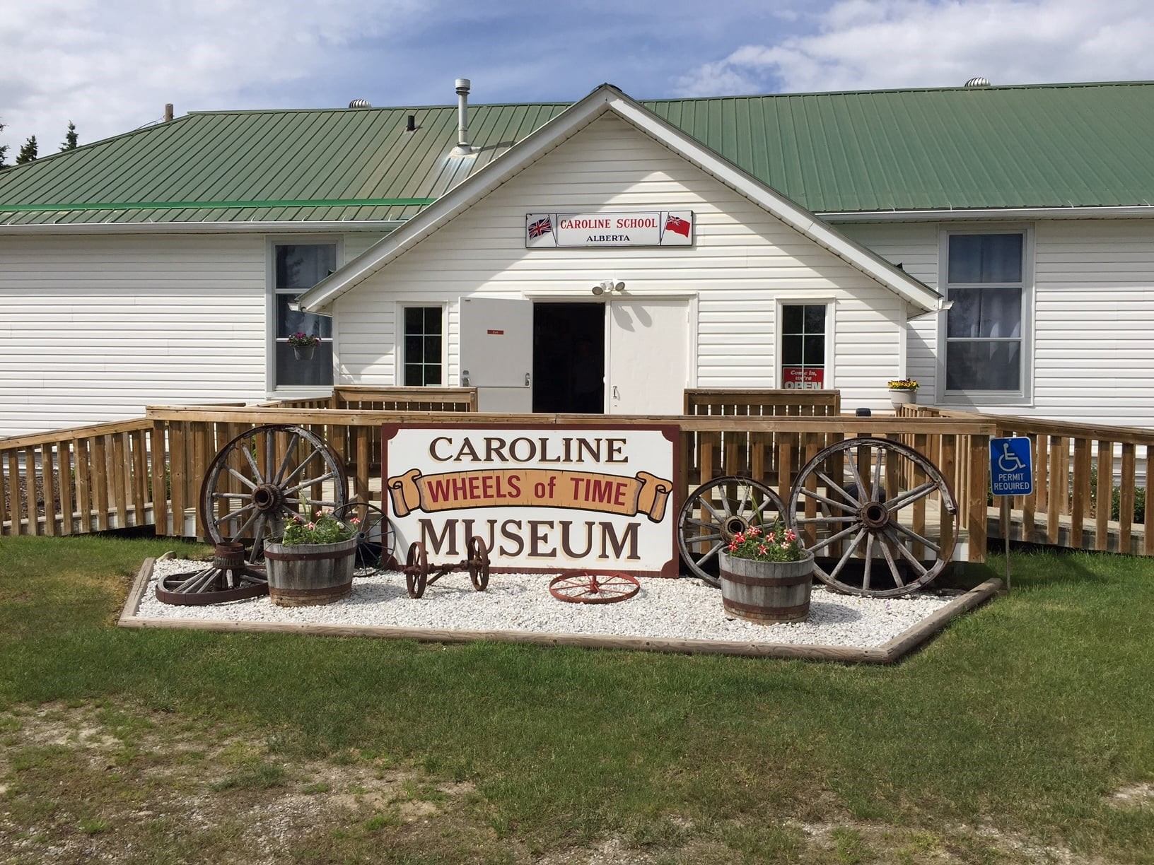Museum entrance with wagon wheels, flower barrels, and a green-roofed building.