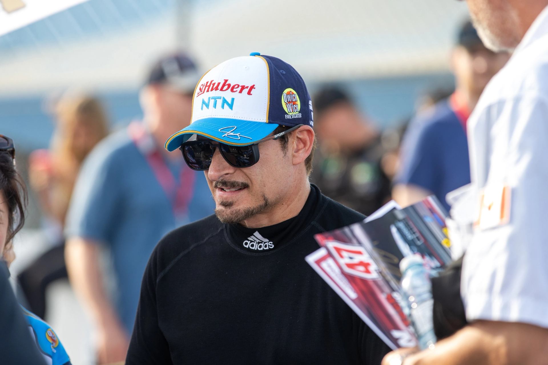 Person in racing gear and cap holding event materials at NASCAR Canada NAPA 300.