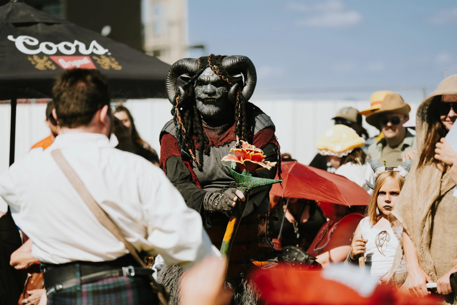 Costumed fantasy character interacting with festivalgoers in a busy outdoor medieval-themed market.