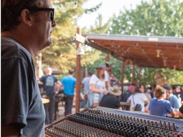 Audience members seated at outdoor event with rows of microphones on stage platform.