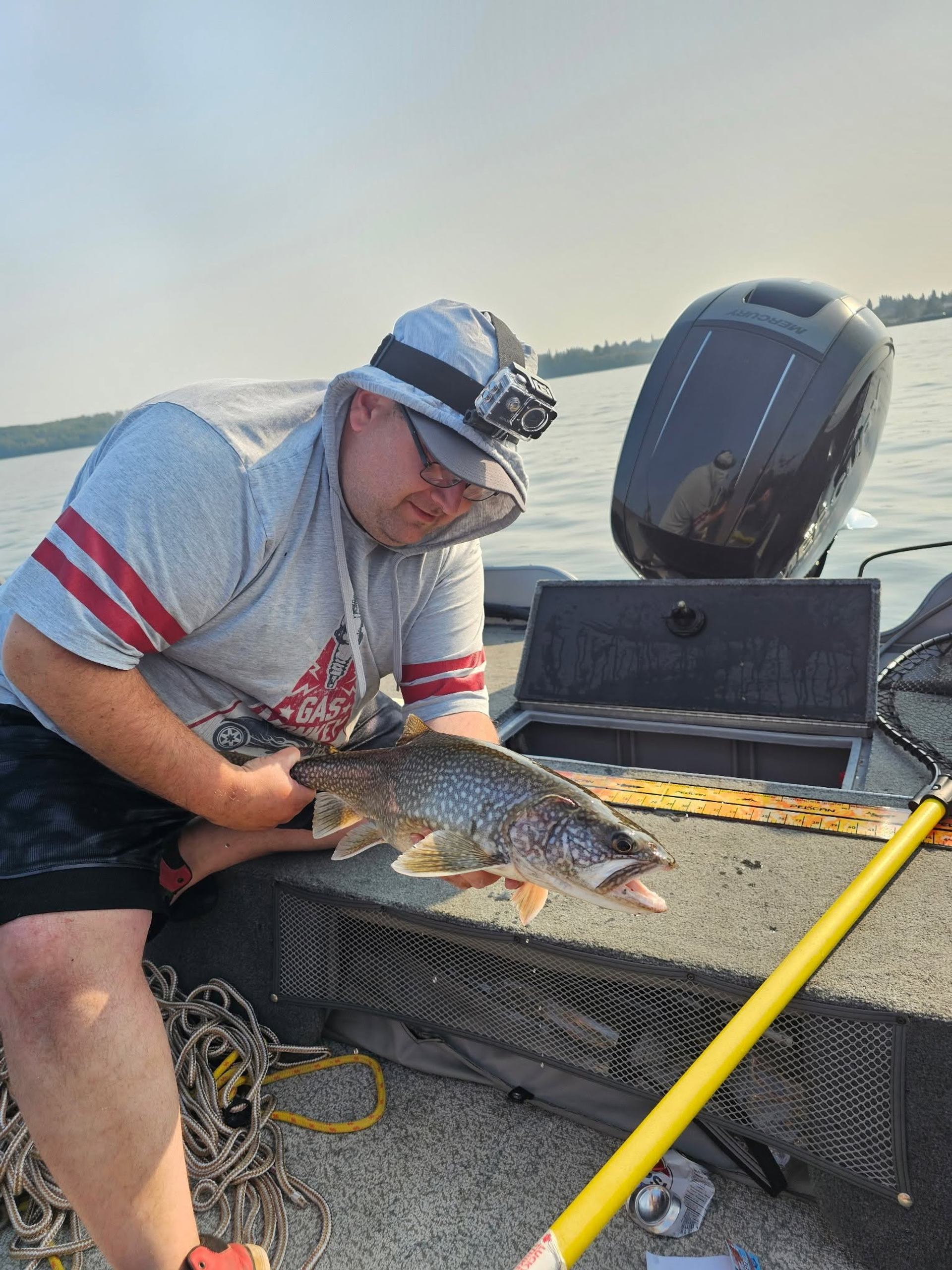 Person on boat holding speckled fish beside measuring board and fishing gear.