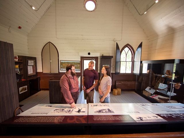 Visitors speaking with an interpreter inside a historic building with displays and tall arched windows.