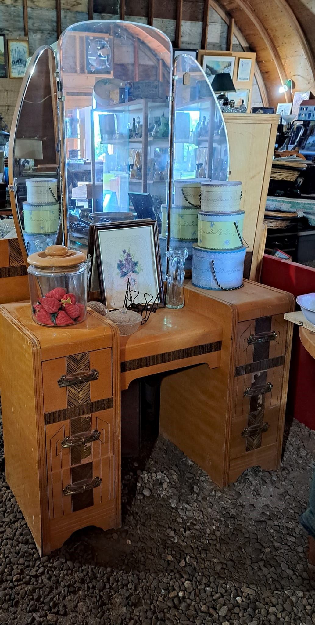 Antique display case and wooden cabinet with framed artwork, glass jars, and wrapped cakes.