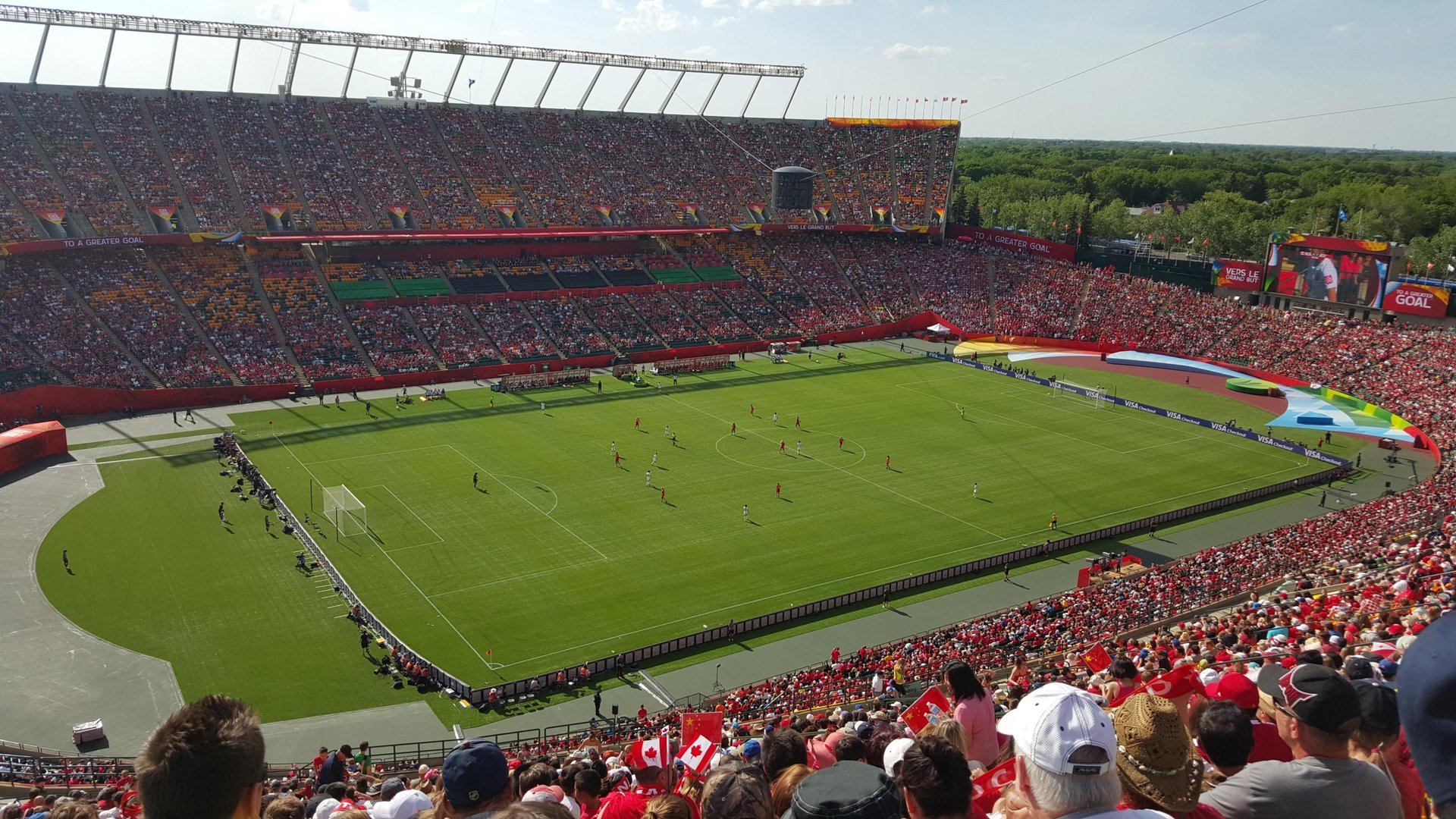 Crowded stadium with soccer match in progress and fans waving Canadian flags.