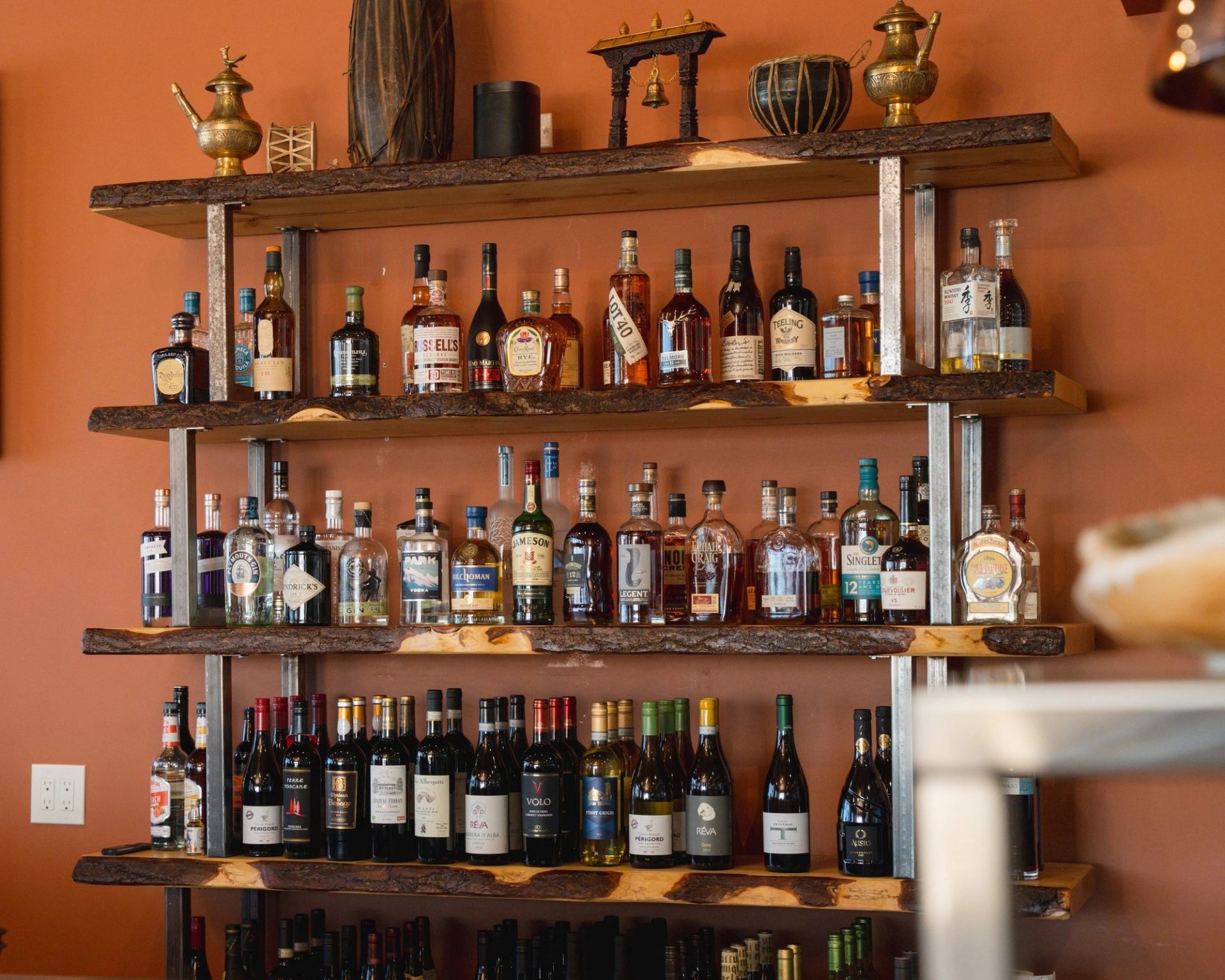 Bottles on restaurant bar shelves with decorative brass serving pitchers and goblets.