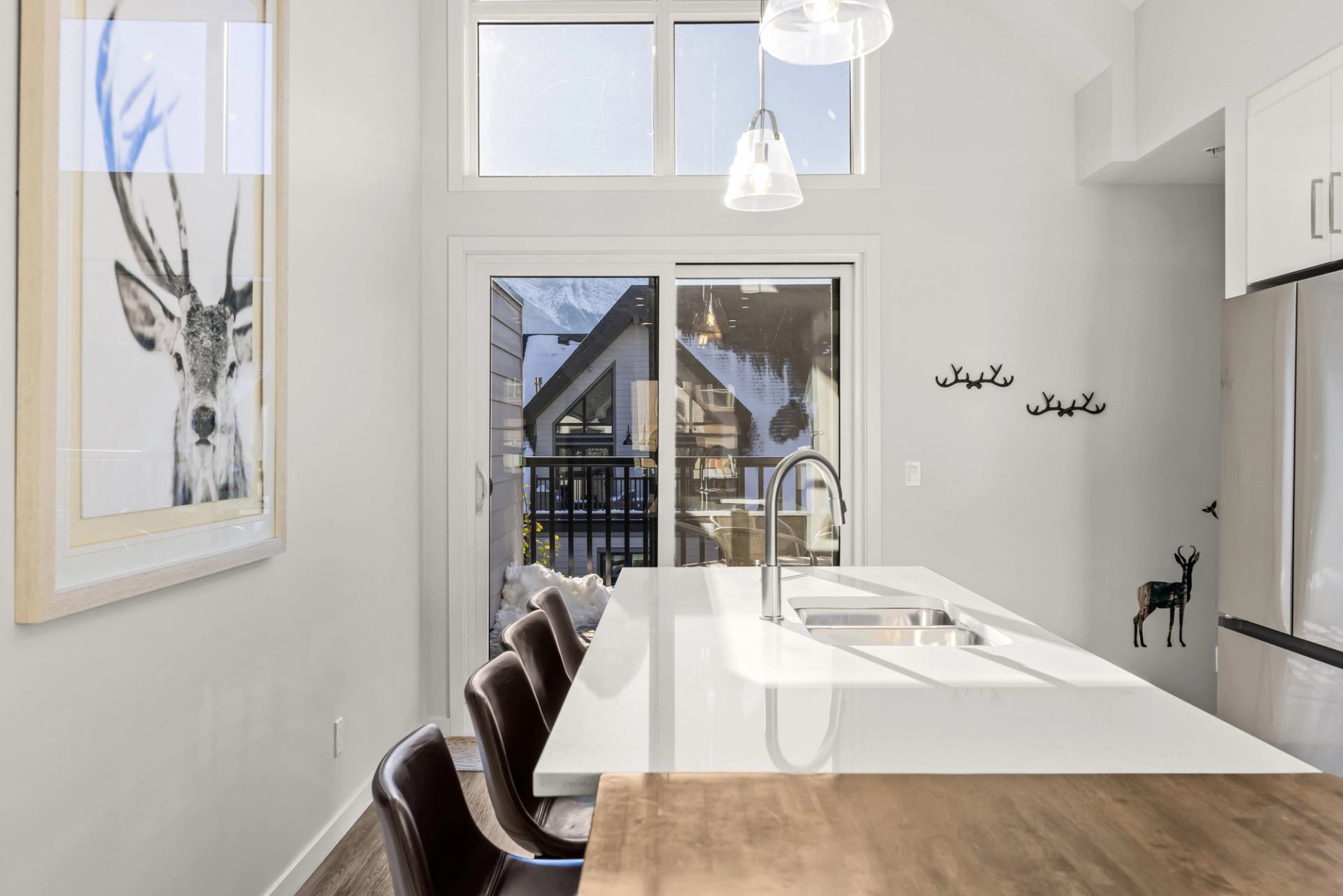 Bright white kitchen with island seating, pendant lights and framed deer artwork.