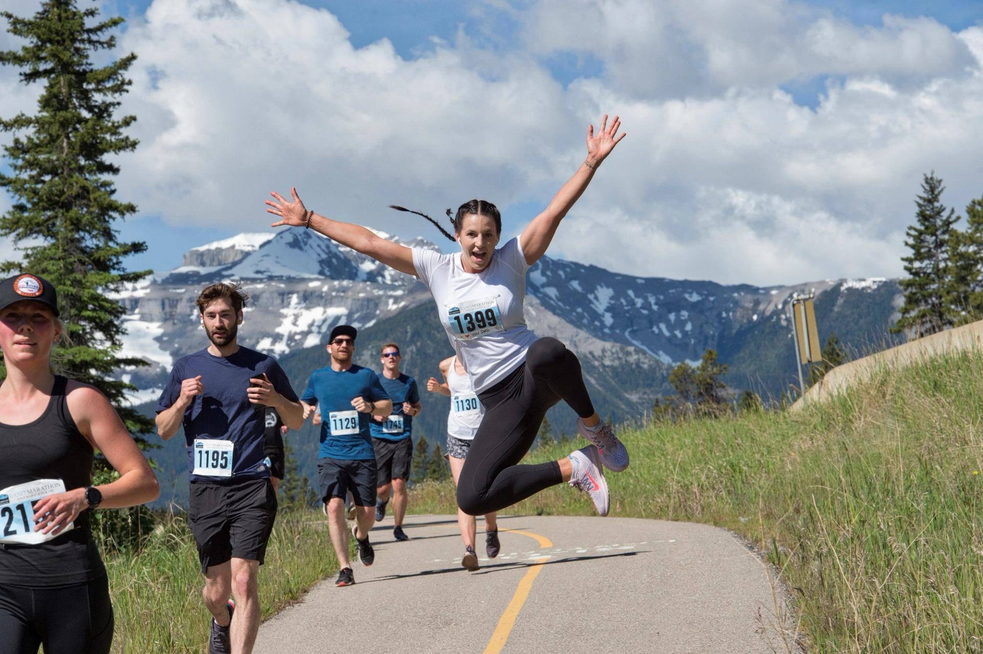 Runners on mountain trail, one jumping with arms raised.