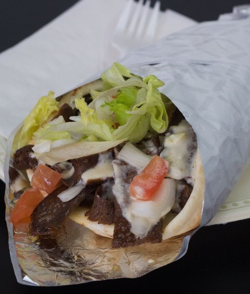 Close-up of a foil-wrapped pita filled with meat, lettuce, tomato, and sauce.