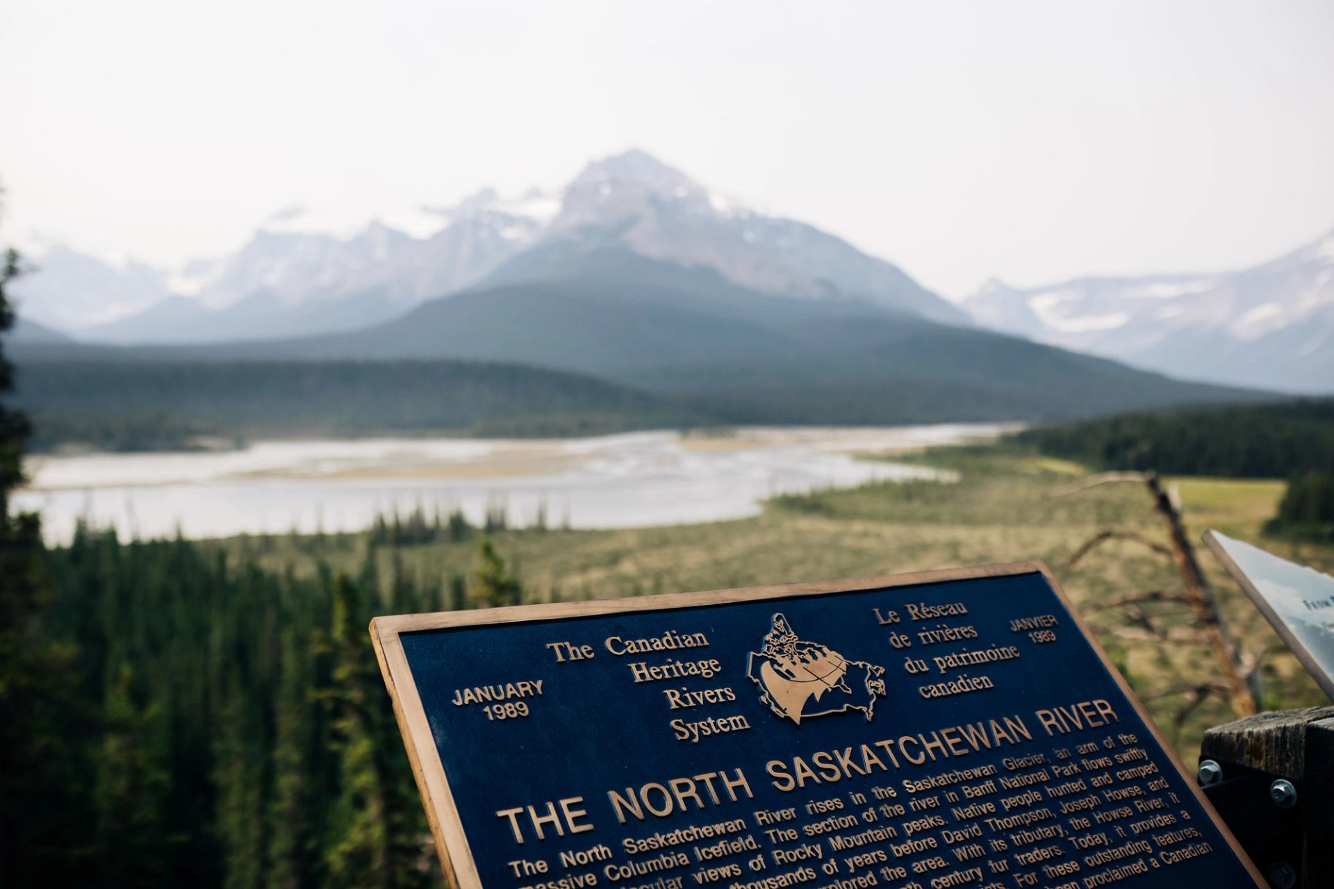 Information plaque for the North Saskatchewan River overlooking forest, river and distant mountains.