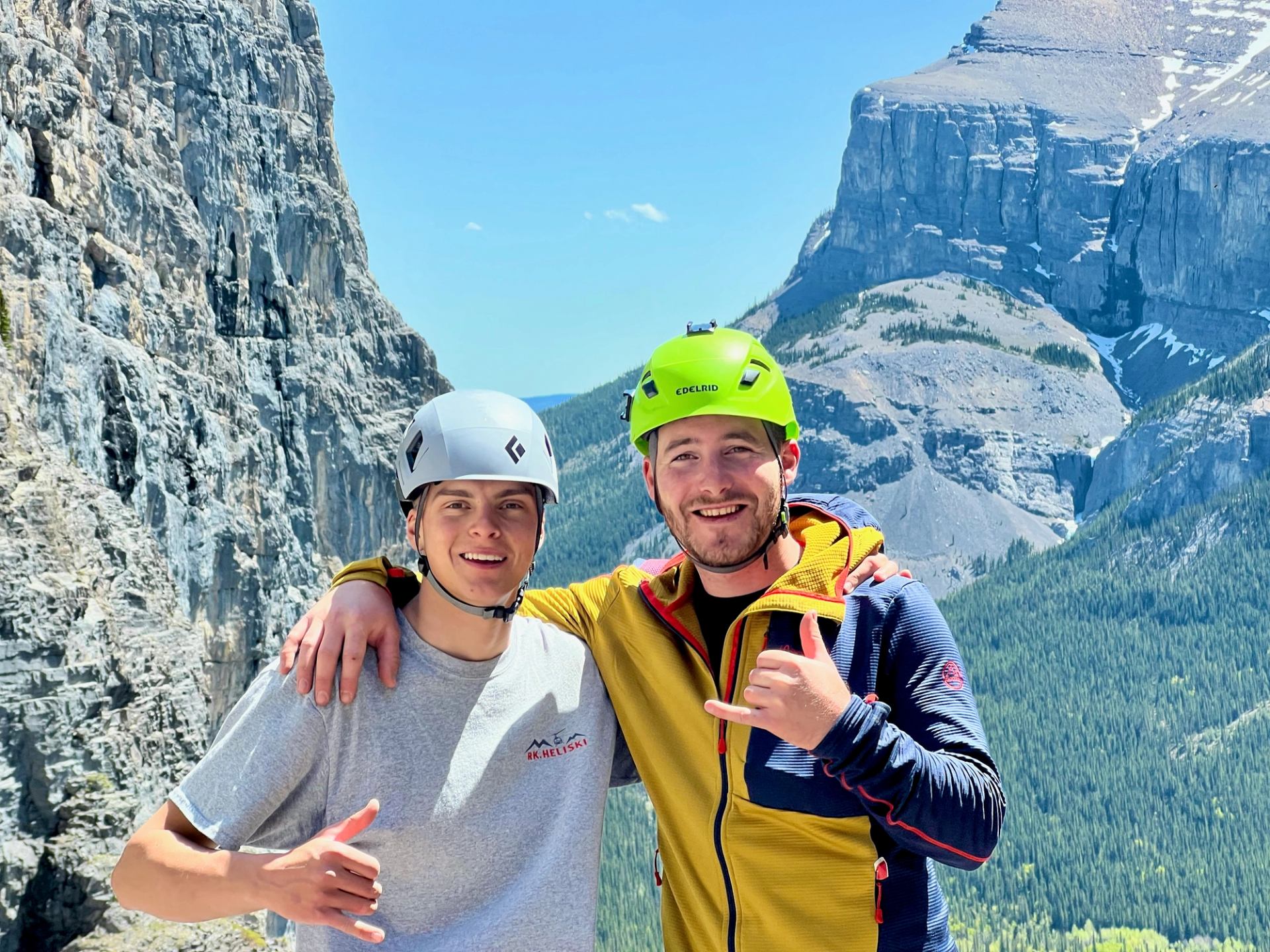 Two climbers posing on a rocky ledge with towering mountains in the background.