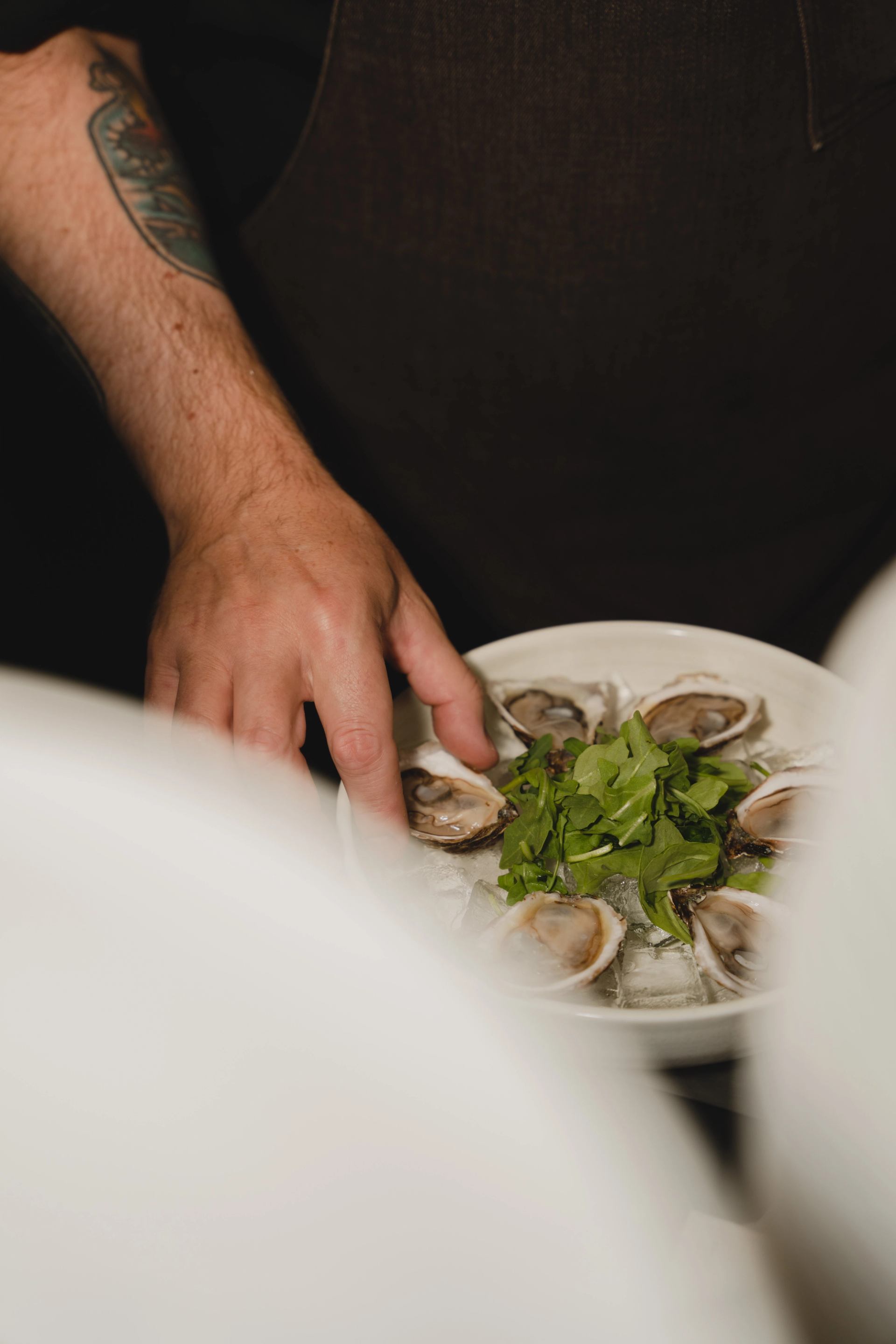 A hand arranging a plate of freshly shucked oysters topped with greens.
