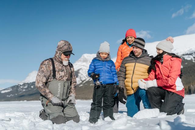 An ice fishing guide helps a young family while they are ice fishing on a frozen lake near Canmore in Kananaskis Country