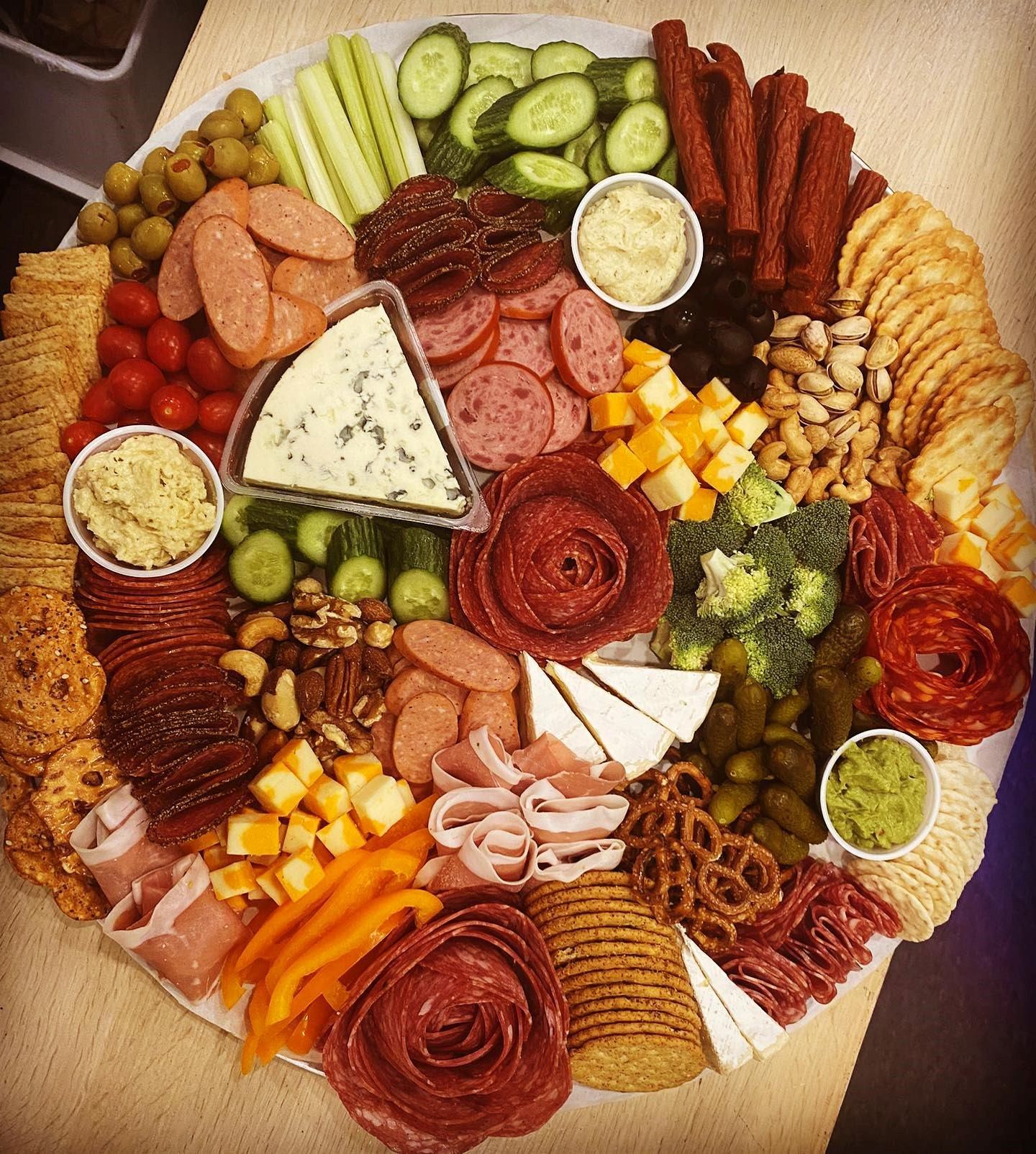 Circular charcuterie board with meats, cheeses, fruits, veggies, and dips.