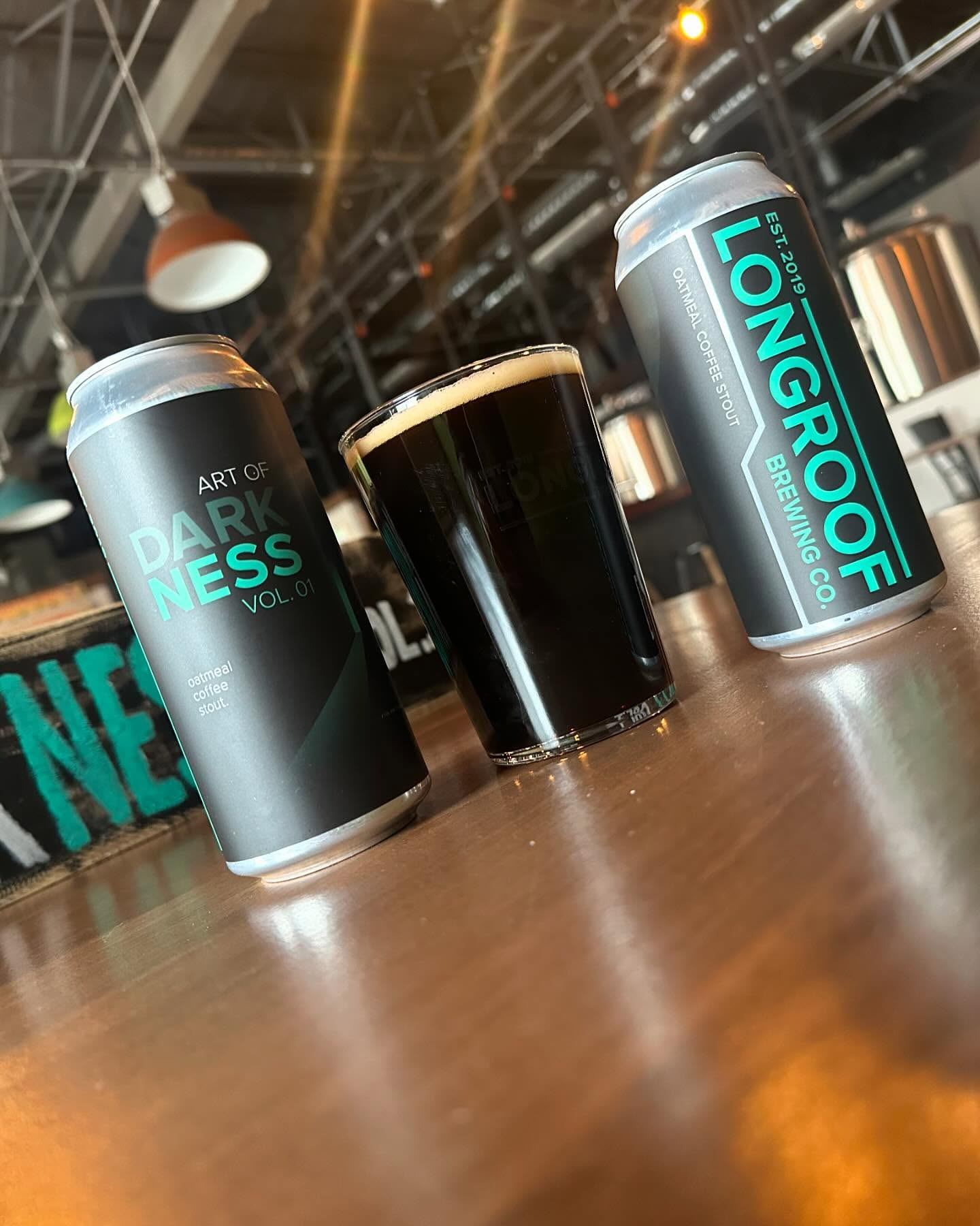 Dark beer poured in a glass with Longroof Brewing cans on a taproom table.
