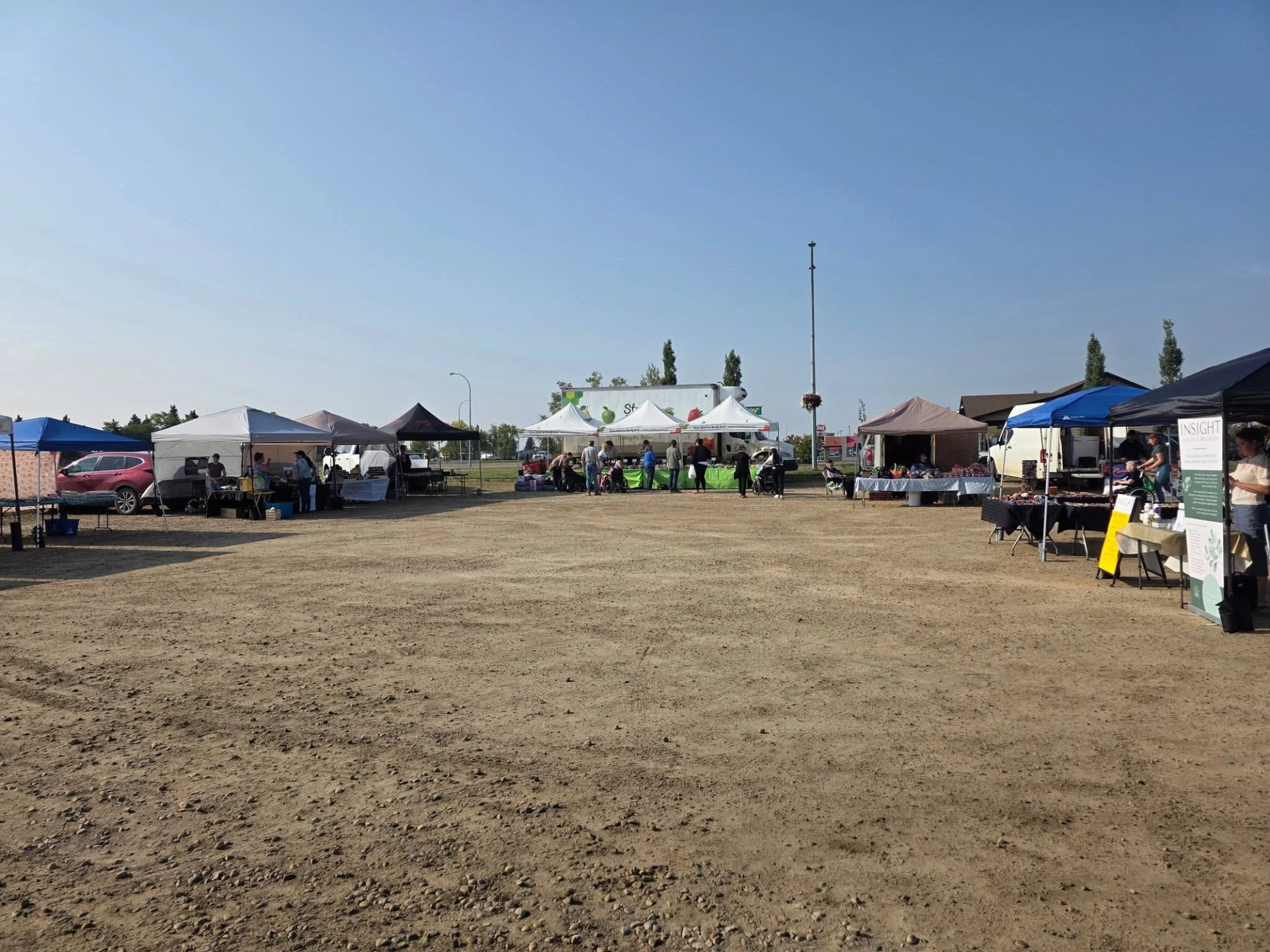 Market tents line an open outdoor space as visitors explore vendors on a sunny day.