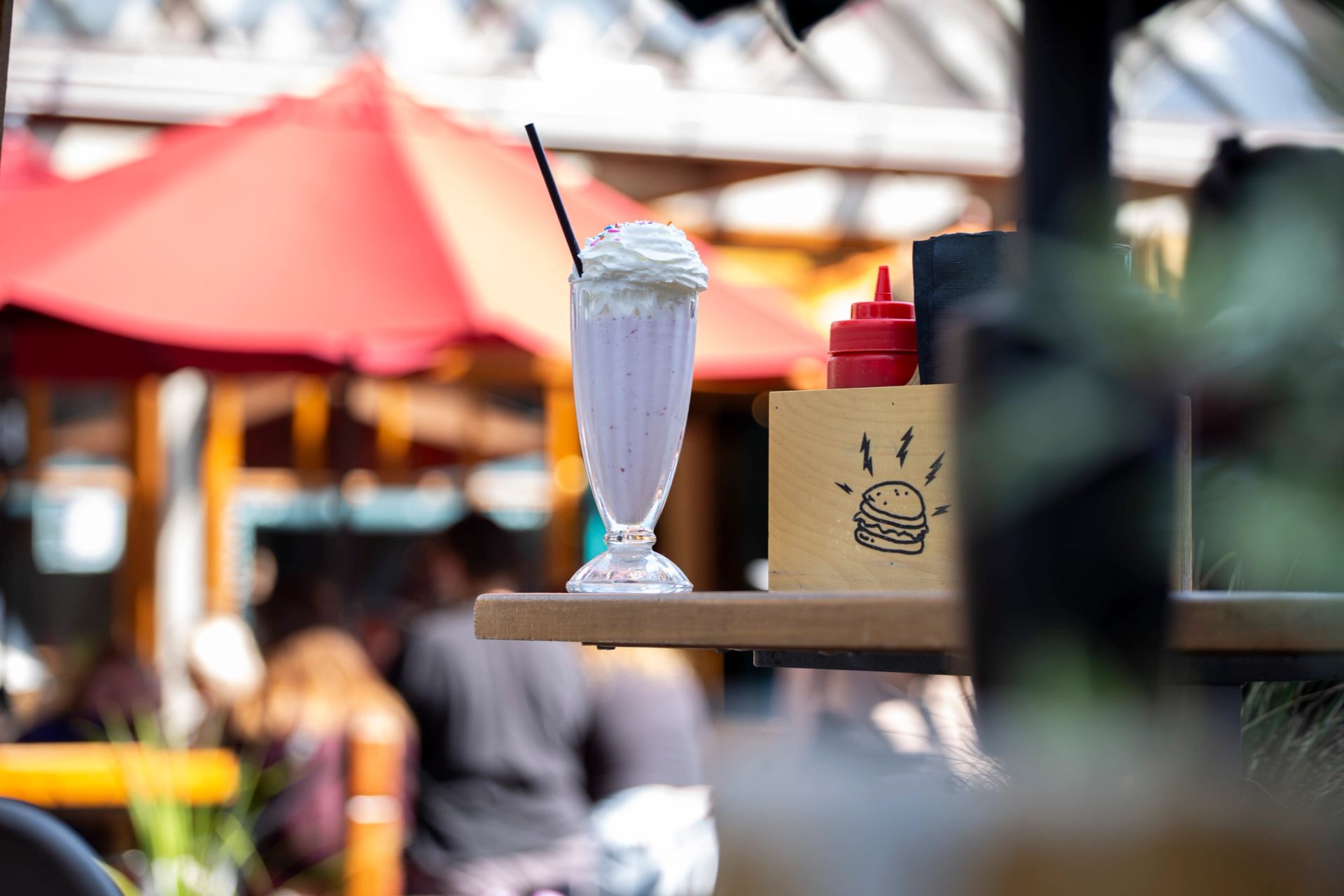A light purple milkshake with whipped cream and sprinkles on an outdoor patio.
